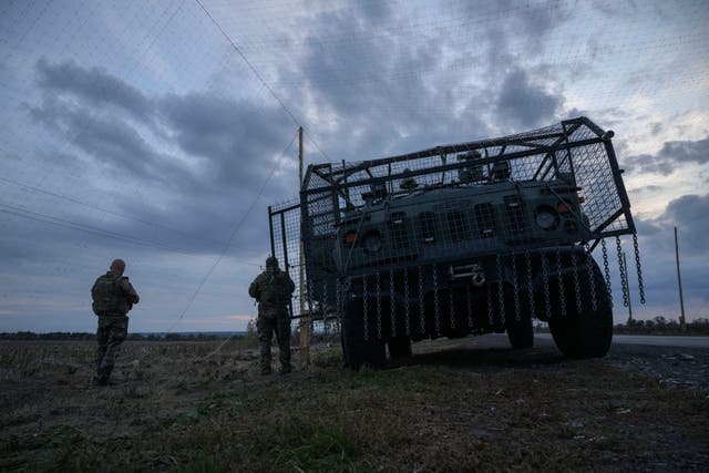 <p>Ukrainian soldiers stand before an armoured military vehicle surrounded by a cage to protect against drone attacks on a road near Oleksandrivka, on 6 October 2025 amid the Russian invasion of Ukraine</p>