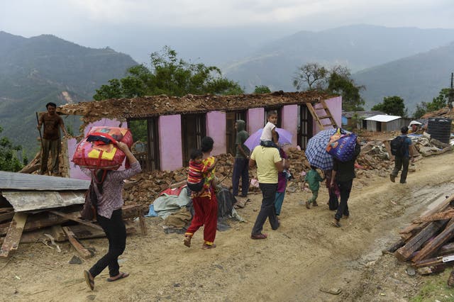 <p>Nepalese residents walk through rain past a destroyed house in Chautara in north-eastern Nepal</p>