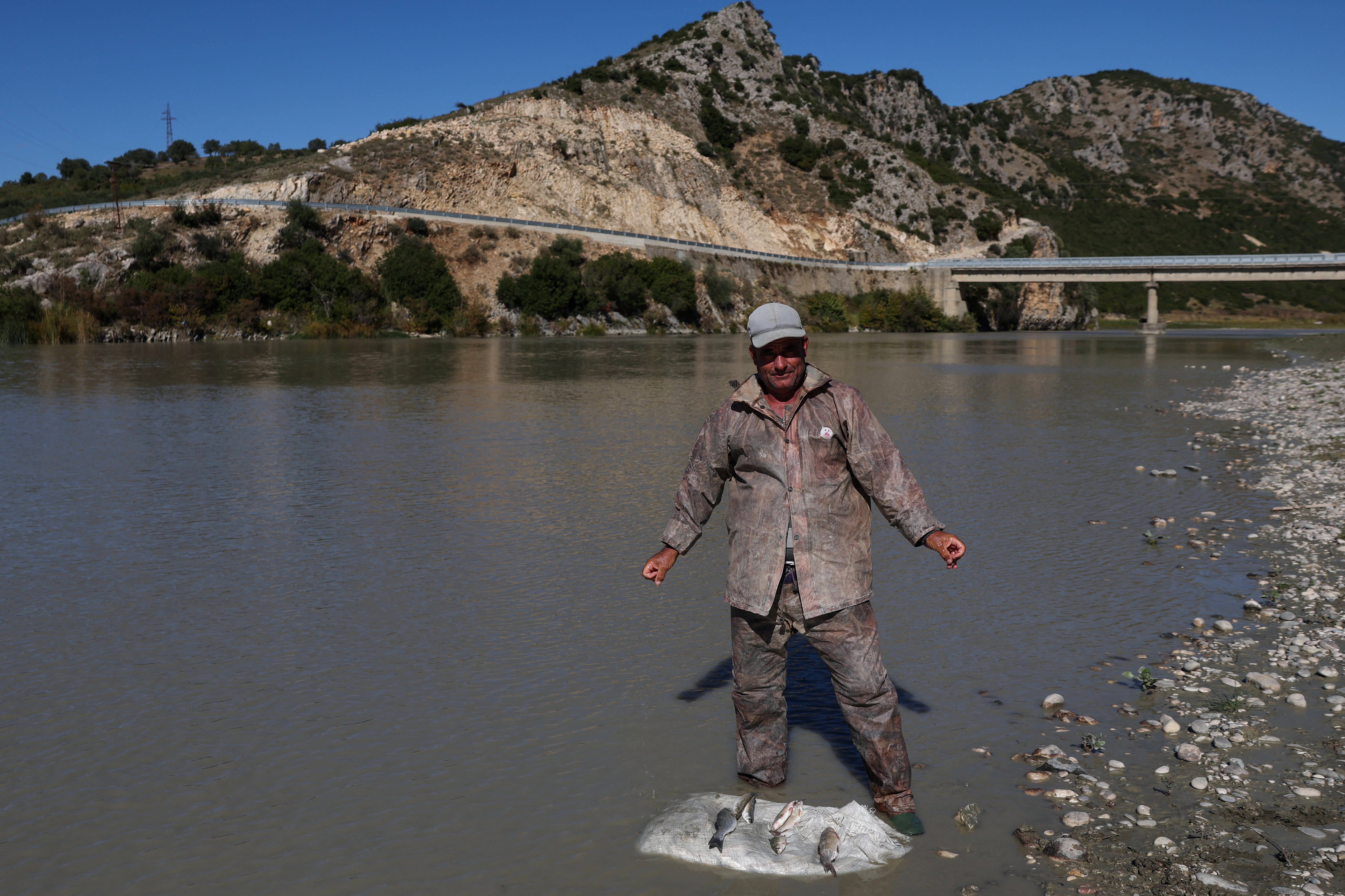 A fisherman stands next to fish in the Vjosa river, recently designated a UNESCO site, near Selenice, Albania