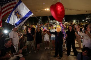 A wearing a mask depicting US president Donald Trump waves an Israeli flag with a yellow ribbon in the center