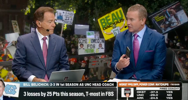 <p>ESPN "College GameDay" host Kirk Herbstreit shows his co-host, Nick Saban, that he is receiving a call from University of North Carolina head football coach Bill Belichick during their live broadcast</p>