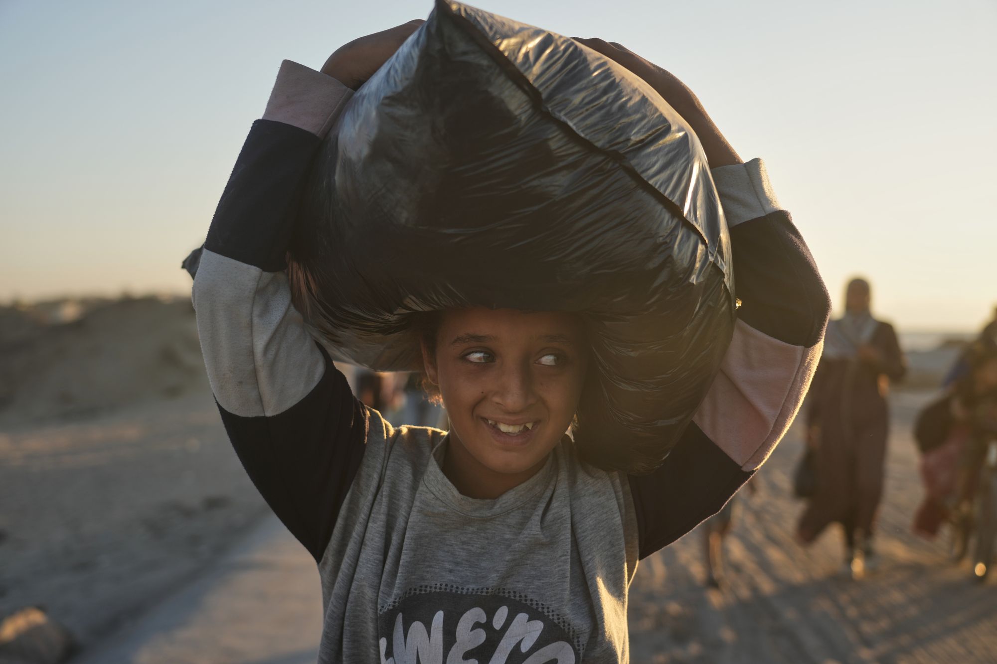 A displaced Palestinian girl carries a bag on her head as she walks along the coastal road near Wadi Gaza in the central Gaza Strip,