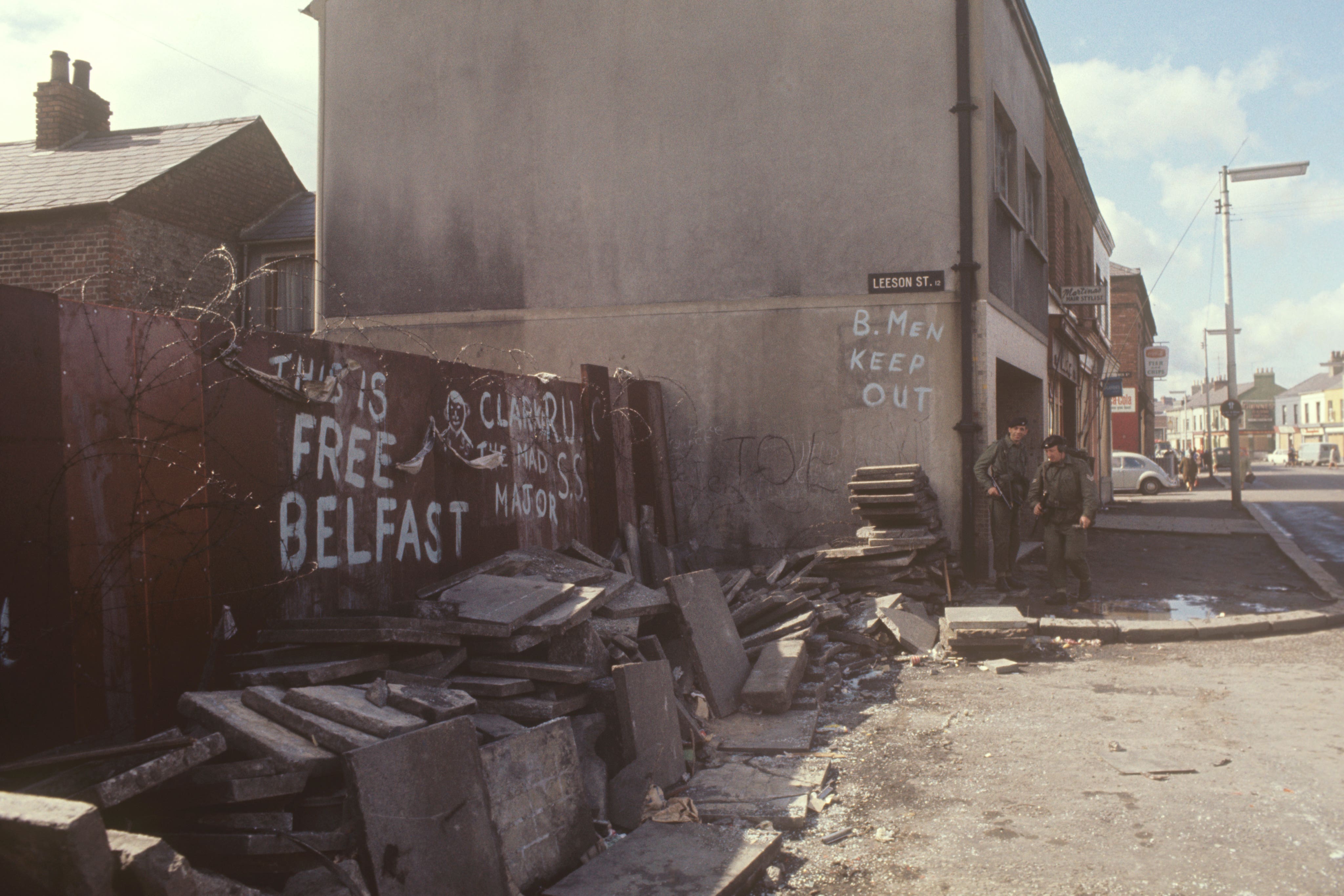 Torn-up paving stones, slogans on a fence and soldiers on guard on a corner of Leeson Street and Falls Road (Archive/PA)
