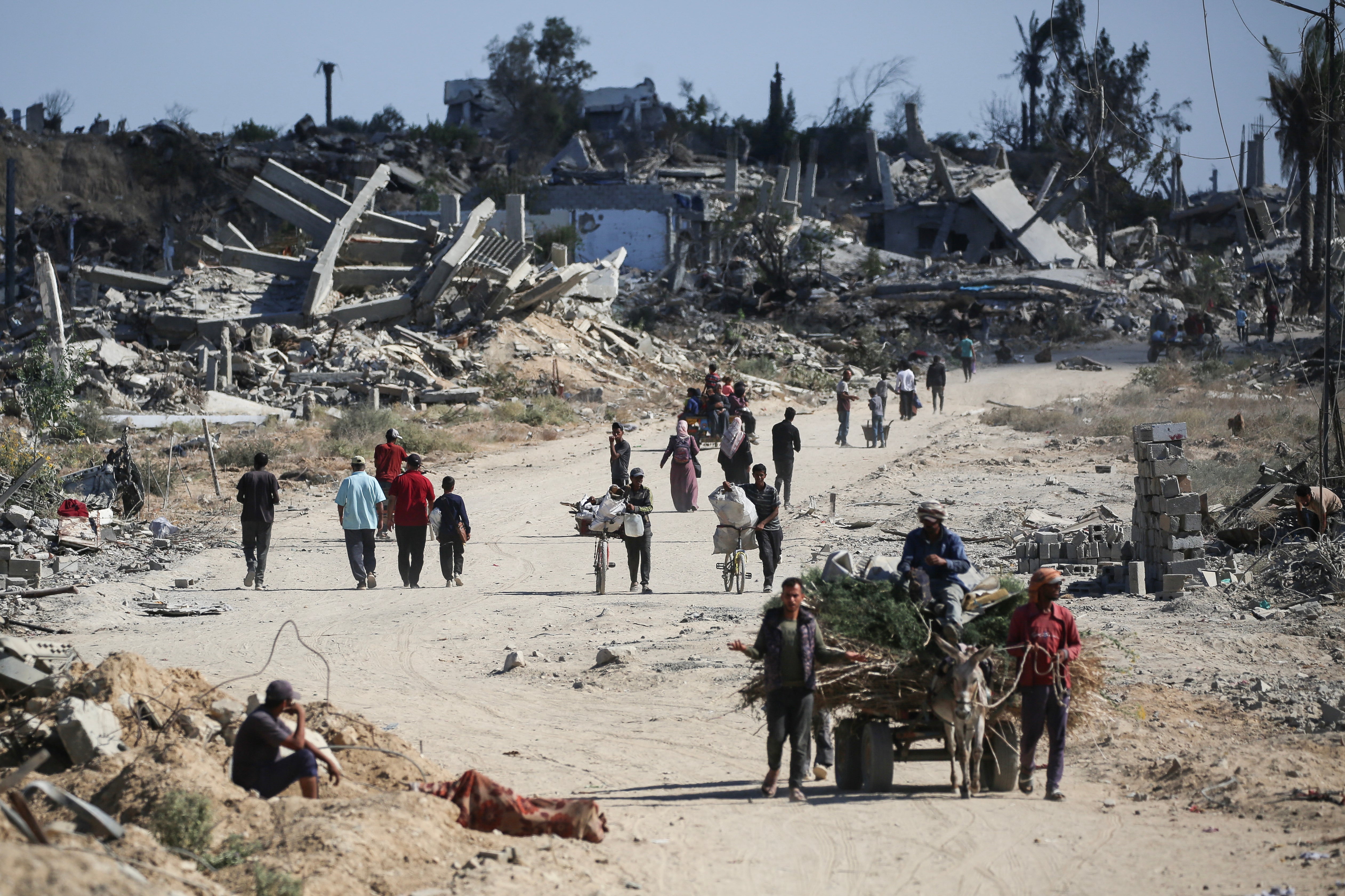 <p>Displaced Palestinians walk past destroyed buildings as they return to their homes in the in al-Zahra area, north of the Nuseirat refugee camp in the central Gaza Strip</p>
