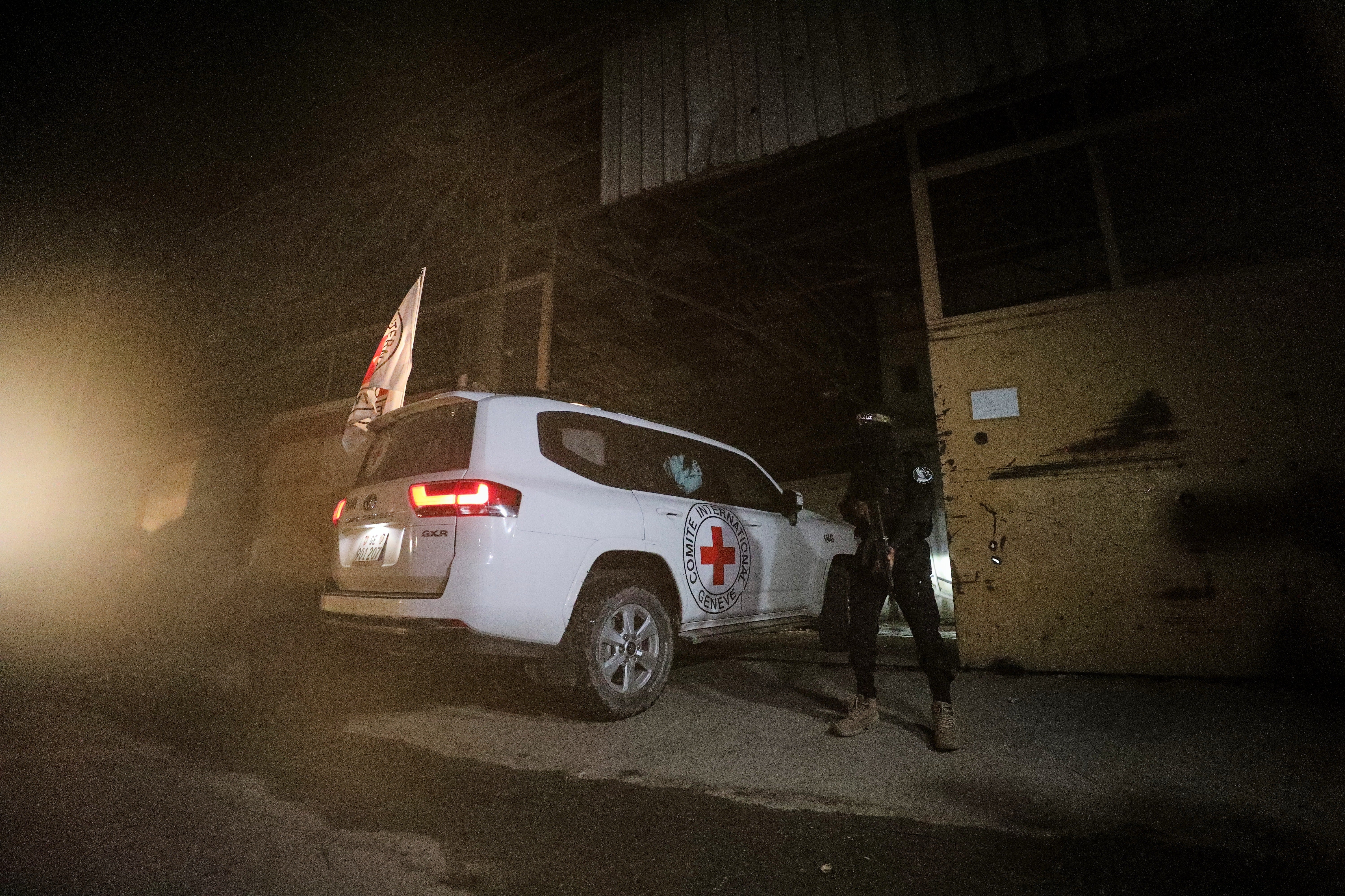 A gunman wearing the uniform of the al-Qassam Brigades, the military wing of Hamas, stands guard as Red Cross vehicles enter a warehouse allegedly to collect coffins containing the bodies of four deceased hostages, in Gaza City, Tuesday, Oct. 14, 2025. (AP Photo/Yousef Al Zanoun)