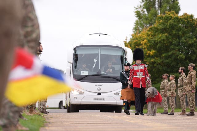 Irish Guards form a guard of honour as a regimental piper and guard in dress uniform with Seamus, a mascot of the regiment, lead coaches carrying Ukrainian soldiers as they depart a British Army training camp (Joe Giddens/PA)