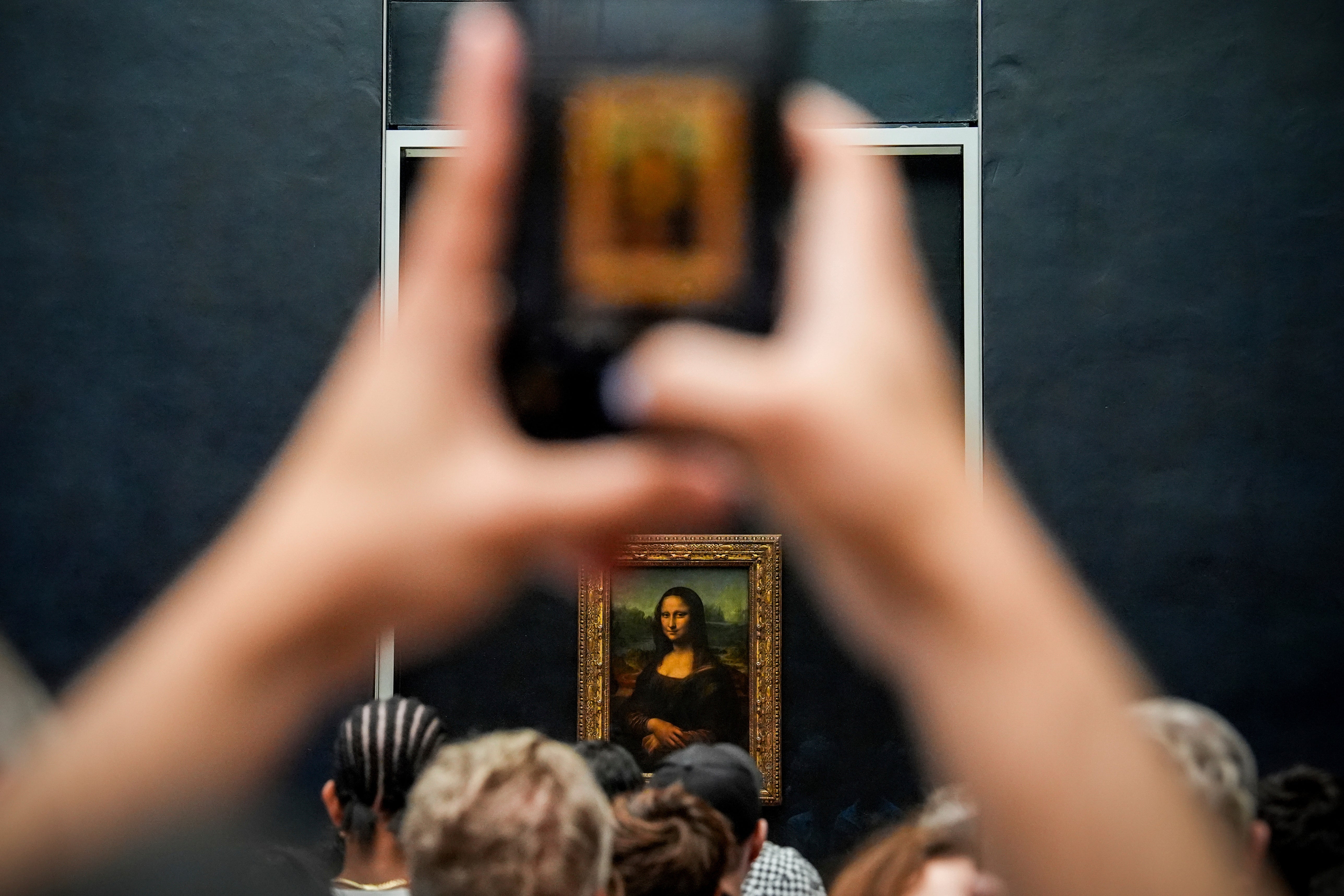 <p>A person photographs Leonardo da Vinci's painting Mona Lisa at the Louvre museum,</p>