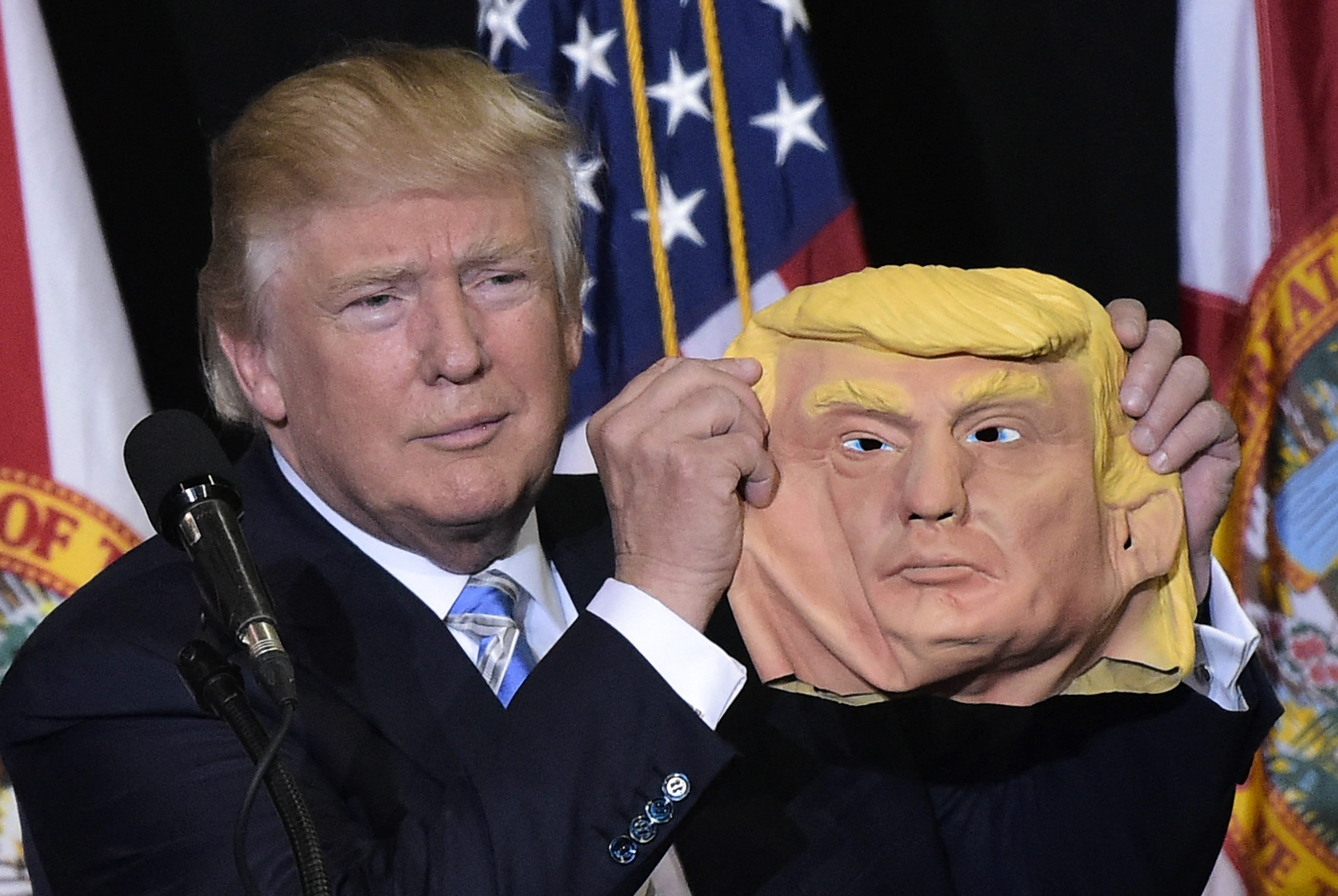 <p>Donald Trump holds a mask of himself in 2016 at Florida rally</p>