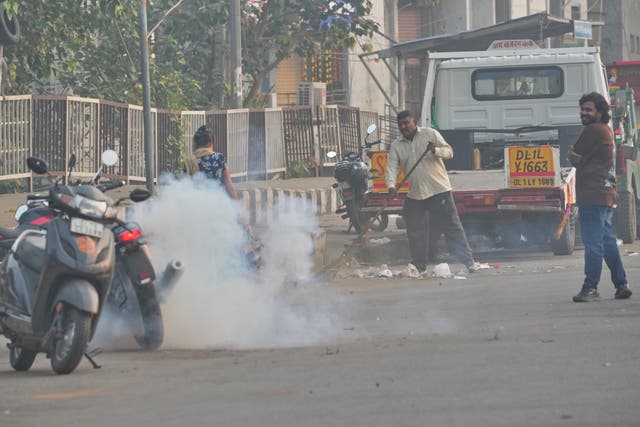 <p>A municipal worker sweeps as a person burns firecrackers amidst morning smog in New Delhi, India</p>