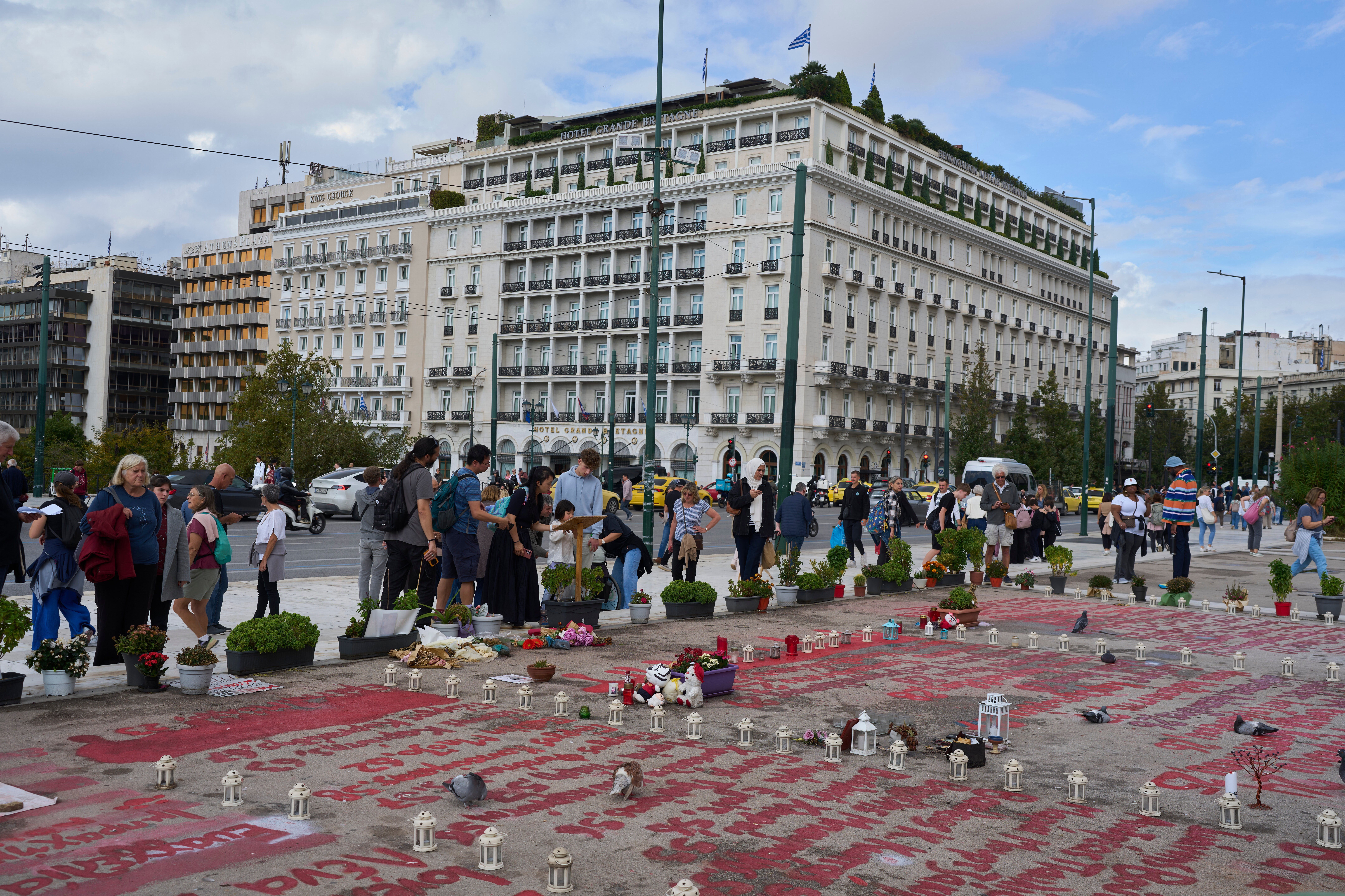 <p>People stand in the square where the names of 57 victims of Greece's deadliest train crash are written on the ground, as Parliament debates regulations to protect the Tomb of the Unknown Soldier monument, which has recently been the focus of demonstrations by victims' relatives. (AP Photo/Petros Giannakouris)</p>