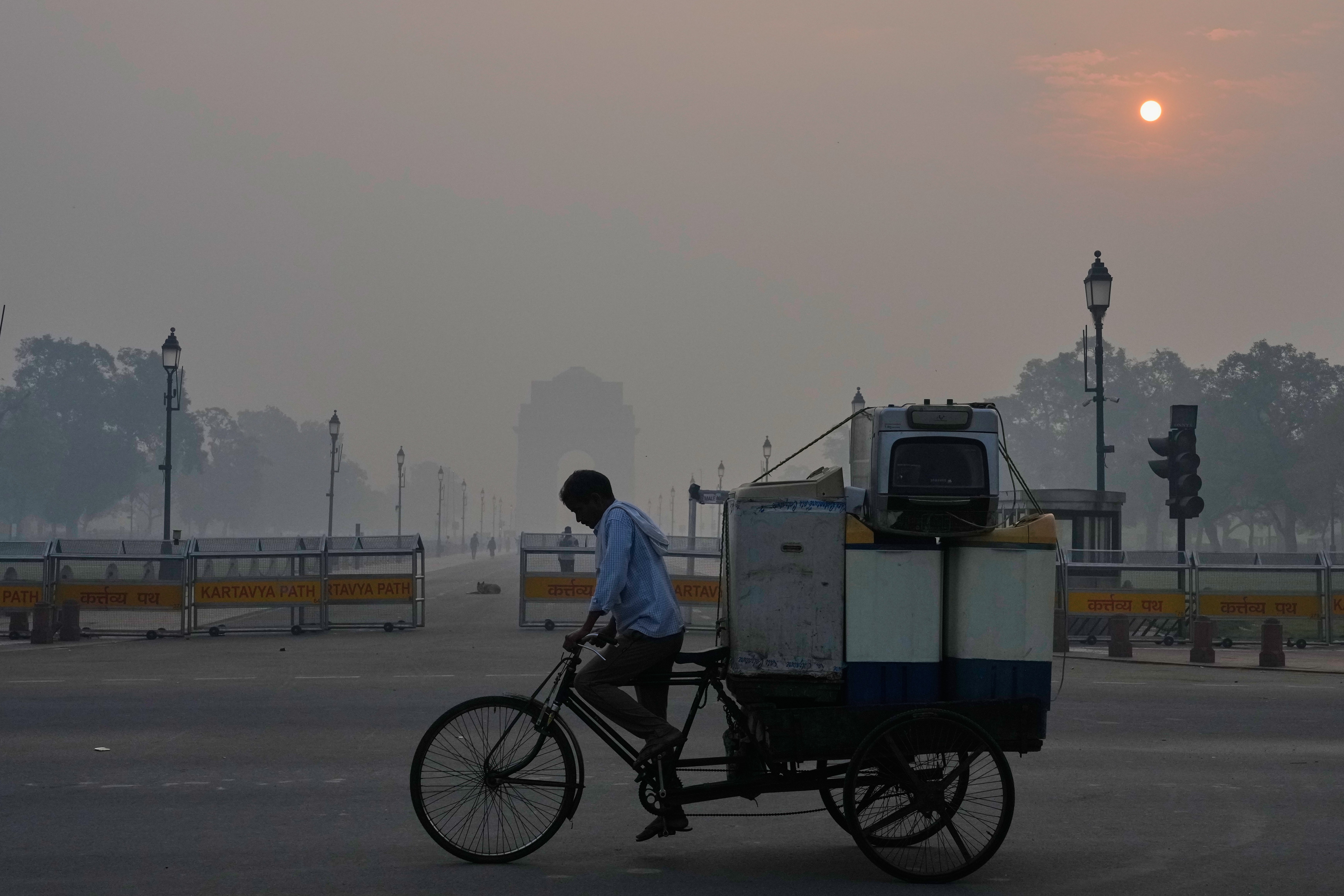A cyclist pedals through morning smog near the India Gate monument as he transports used home appliances a day after Diwali festival in New Delhi, India, Tuesday, Oct. 21, 2025. (AP Photo/Manish Swarup)