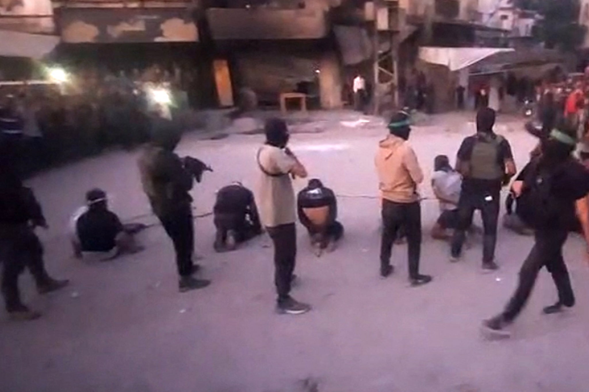 This image grab from a handout video released by the Hamas-run al-Aqsa TV's Telegram channel on October 13, 2025, shows armed Hamas fighters standing behind blindfolded, bound and kneeling men as a crowd surrounds them in a street in Gaza City.
