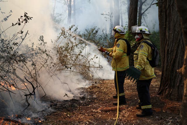 <p>A member of the NSW Rural Fire Service holds a fire hose during a hazard reduction burn in Dural, Australia</p>