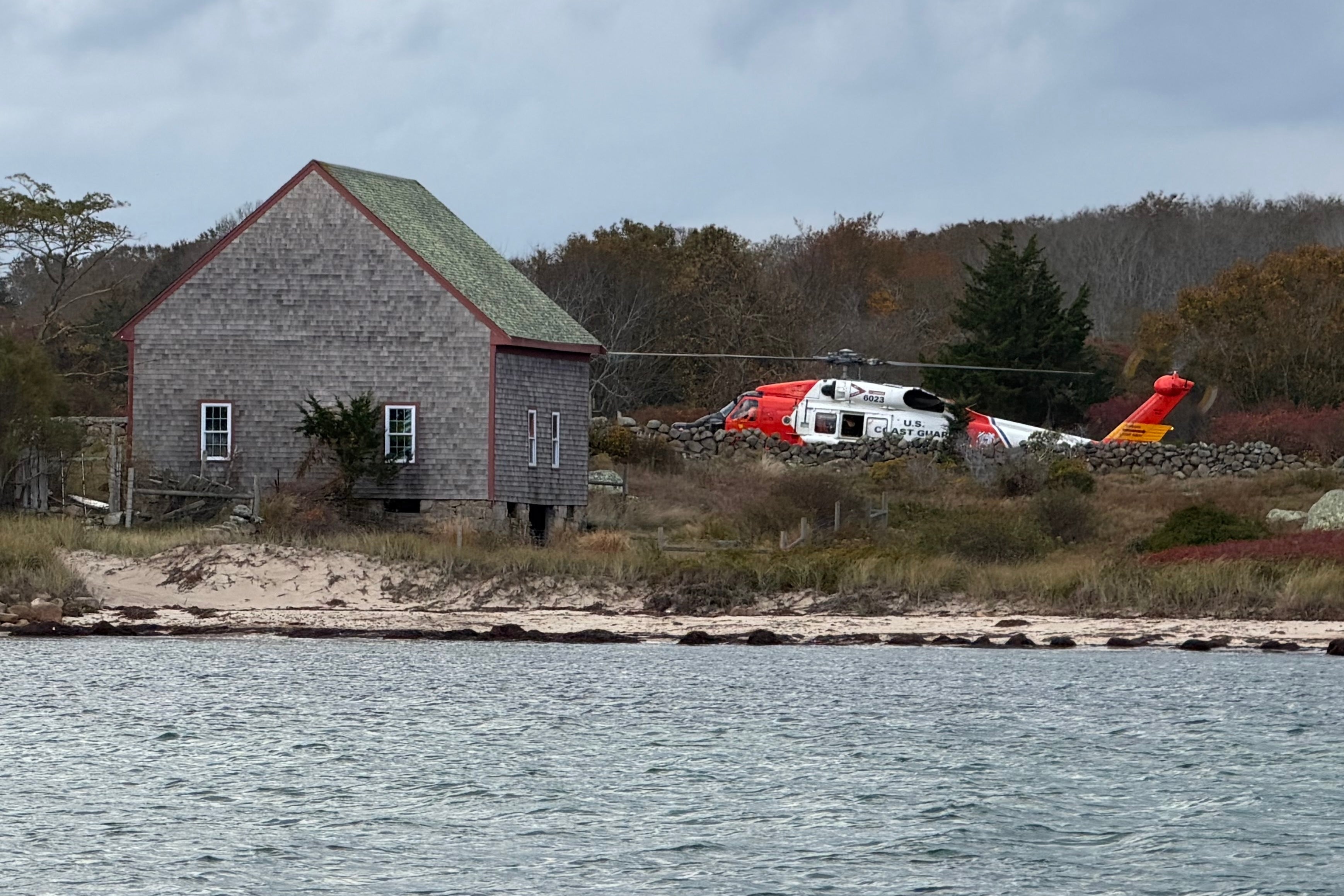Um helicóptero da Guarda Costeira dos EUA se aproxima de Notion Island, Massachusetts, quarta-feira, 22 de outubro de 2025, onde um casal e seu filho adulto foram resgatados dois dias depois que seu barco pegou fogo e nadou até a costa. (Guarda Costeira dos EUA via AP)
