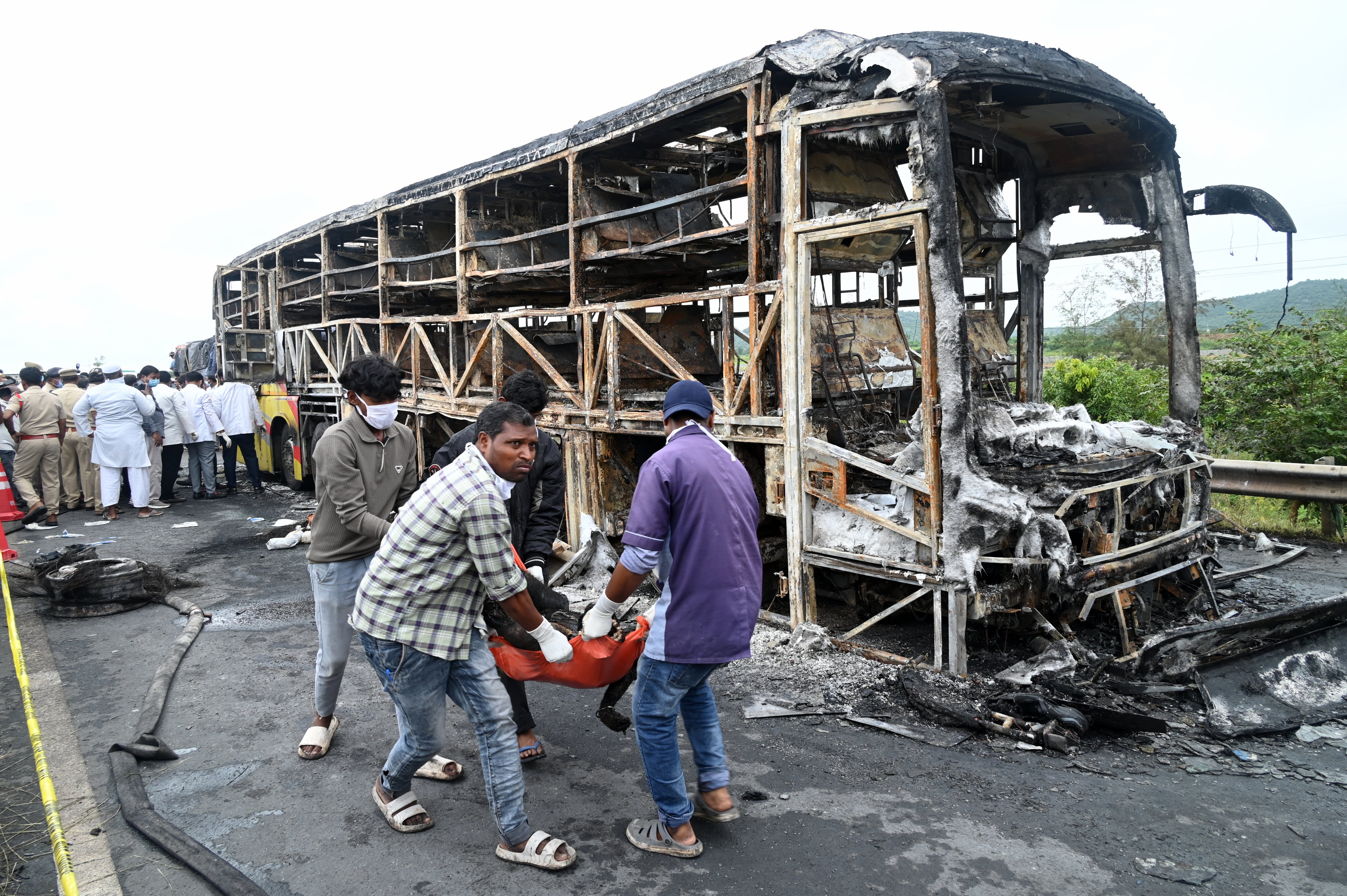 Volunteers remove a dead body from the debris of a passenger bus which caught fire early Friday after a collision with a motorbike on a highway, in Chinnatekuru village, near Kurnool district in Andhra Pradesh state, India