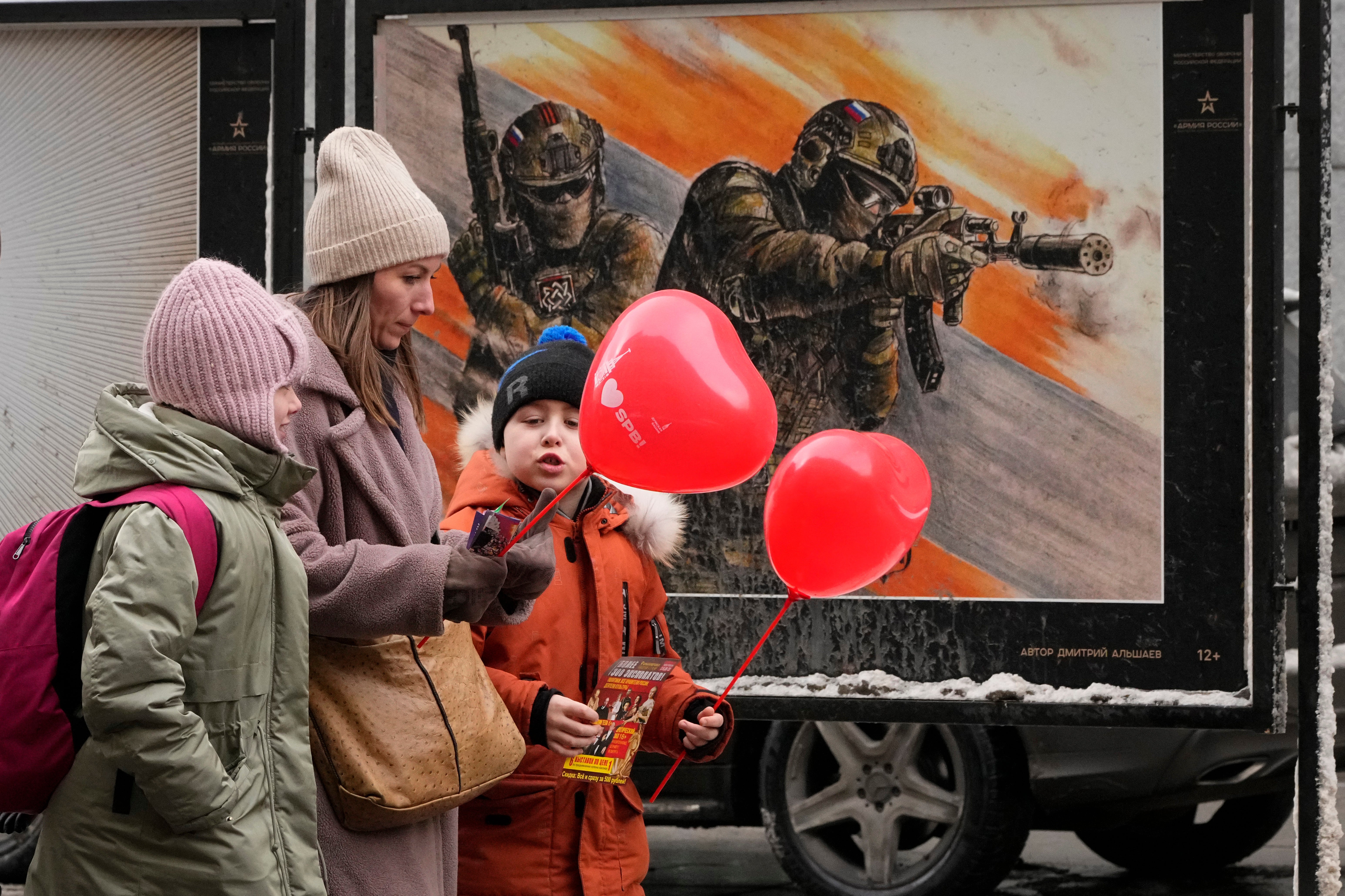 Uma mulher com dois filhos passa por uma exposição de pôsteres militares 'Juntos para a Vitória' dedicados ao exército russo em São Petersburgo, Rússia, sexta-feira, 14 de fevereiro de 2025. (AP Photo / Dmitry Lavotsky, Arquivo)