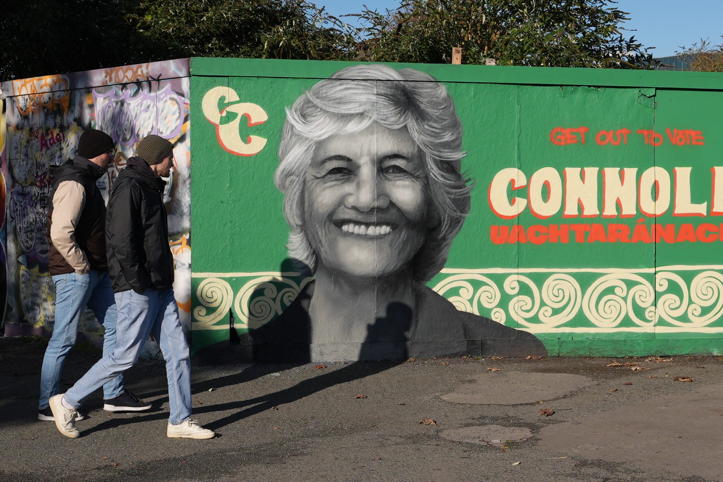 People walk past a mural of Catherine Connolly by artist Emmalene Blake on South Dock Road in Dublin, as counting continues in Ireland’s presidential election to replace Michael D Higgins, who has served the maximum two seven-year terms (Niall Carson/PA)
