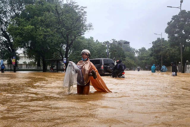 <p>A woman wearing a raincoat wades through a flooded street in Hue, Vietnam</p>