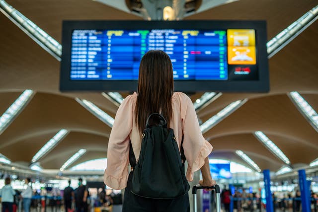<p>rear view of businesswoman standing in front of departure ariival board of international airport looking at the flight information board</p>