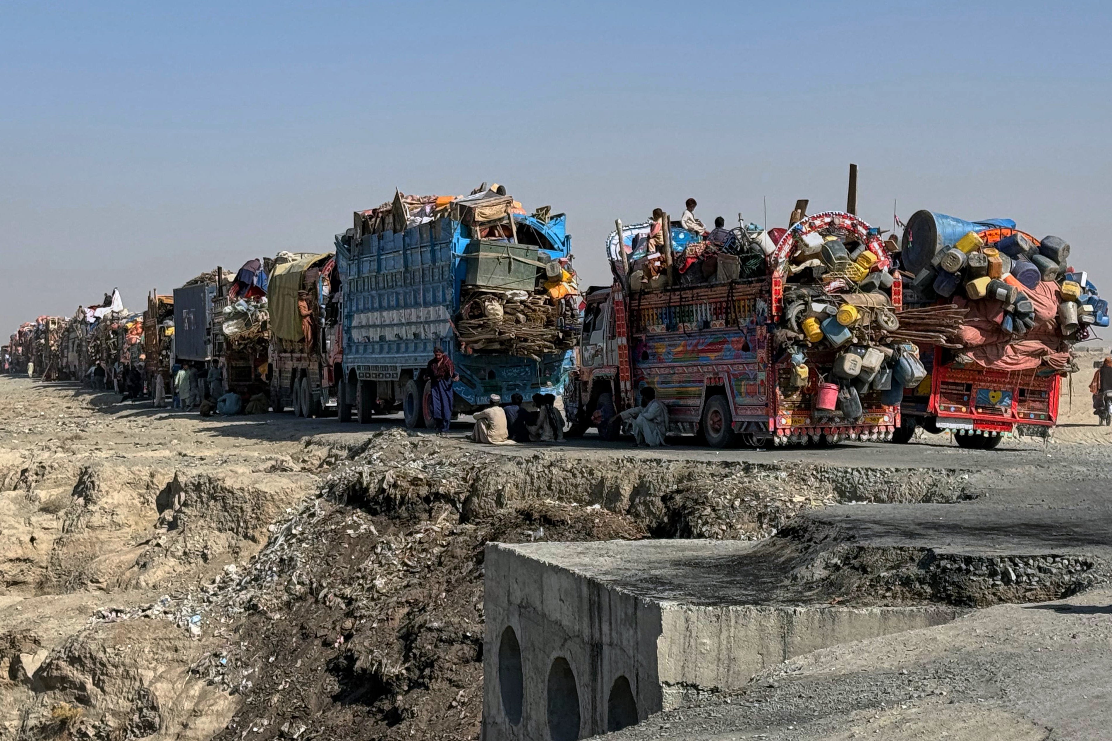 Afghan refugees sit beside trucks loaded with their belongings as they wait their turn to leave for their homeland through a border crossing point