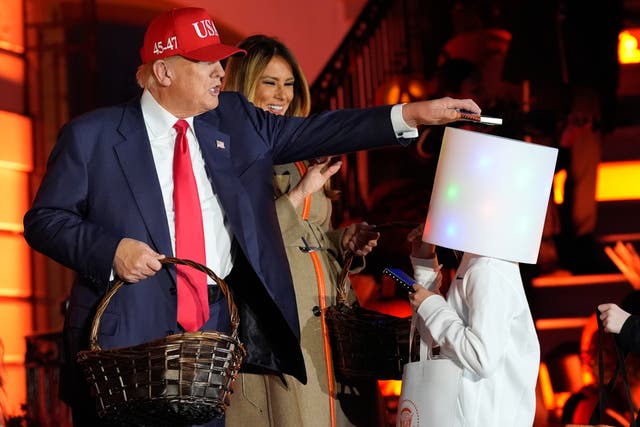 <p>President Donald Trump places a bar of candy on top of a child's costume at the White House Halloween event</p>