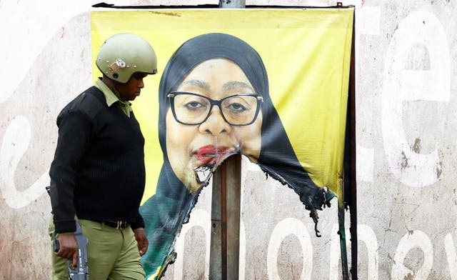 <p>A Tanzanian riot police officer walks past a vandalised campaign poster of President Samia Suluhu Hassan.</p>