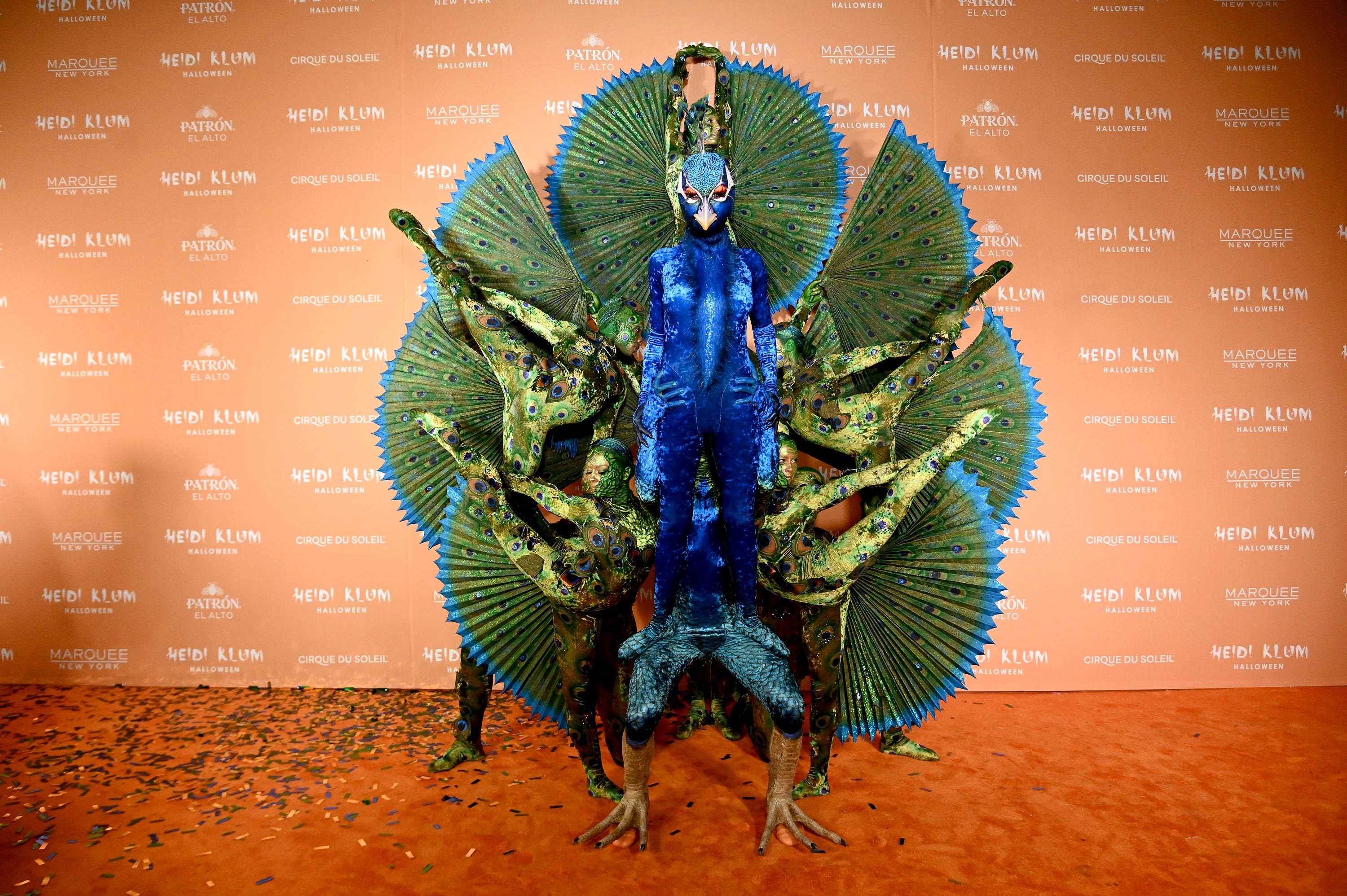 An orchestra of Cirque du Soleil dancers to behind her, while they donned green bodysuits and had painted faces reminiscent of a peacock’s plume.