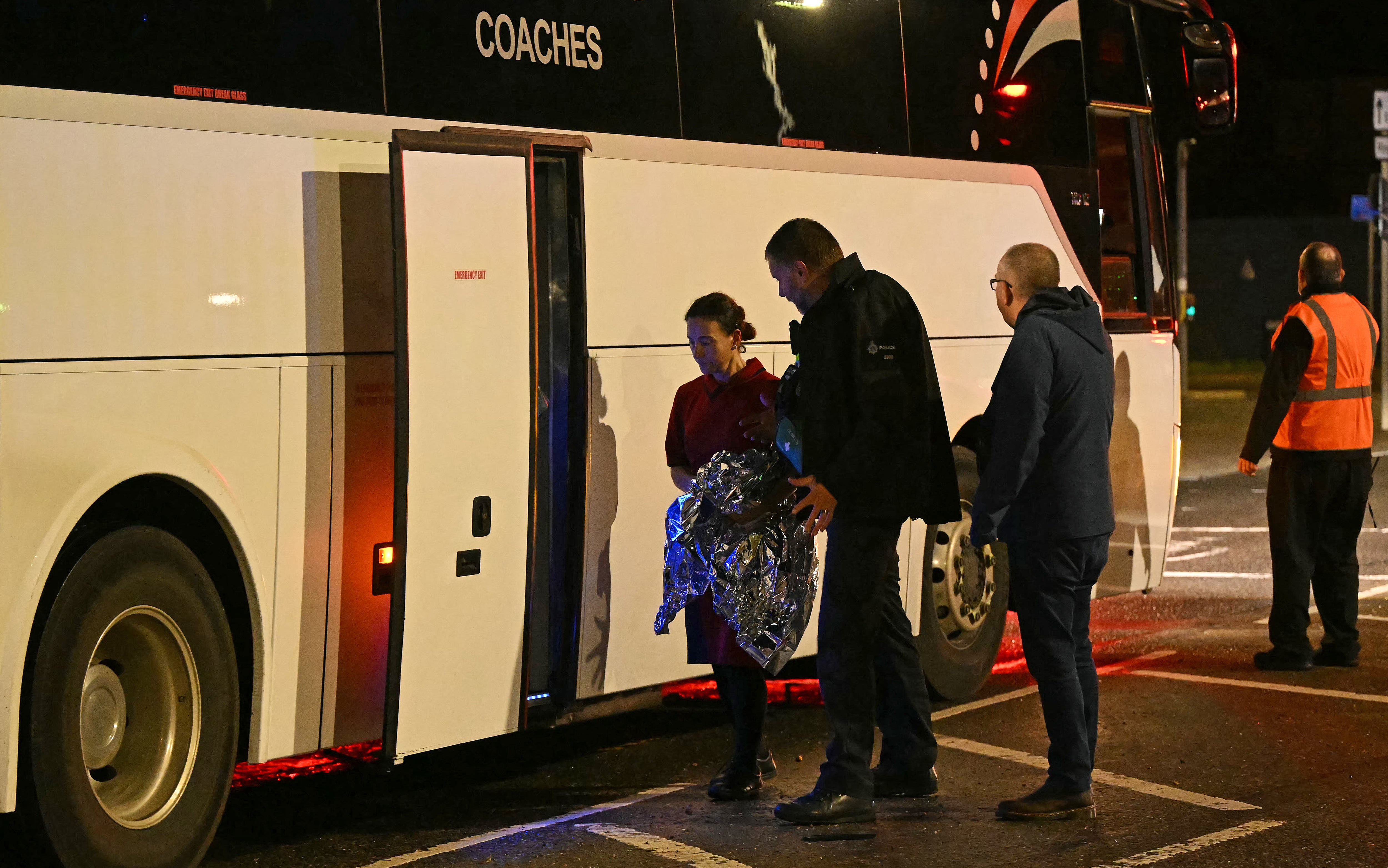 A police officer helps a person carrying a foil blanket onto a couch