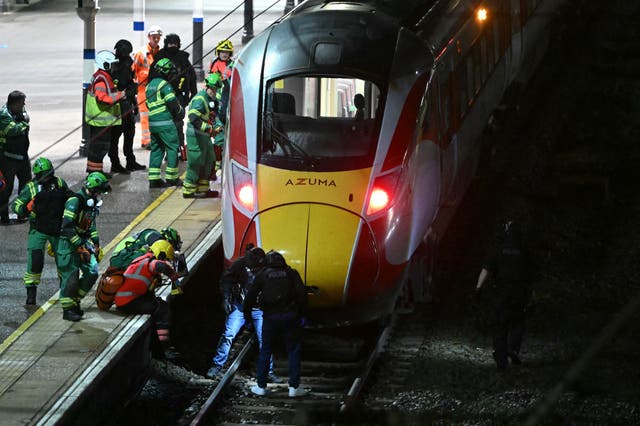 <p>Police officers and members of the emergency services search the track beneath an LNER train at Huntingdon station</p>