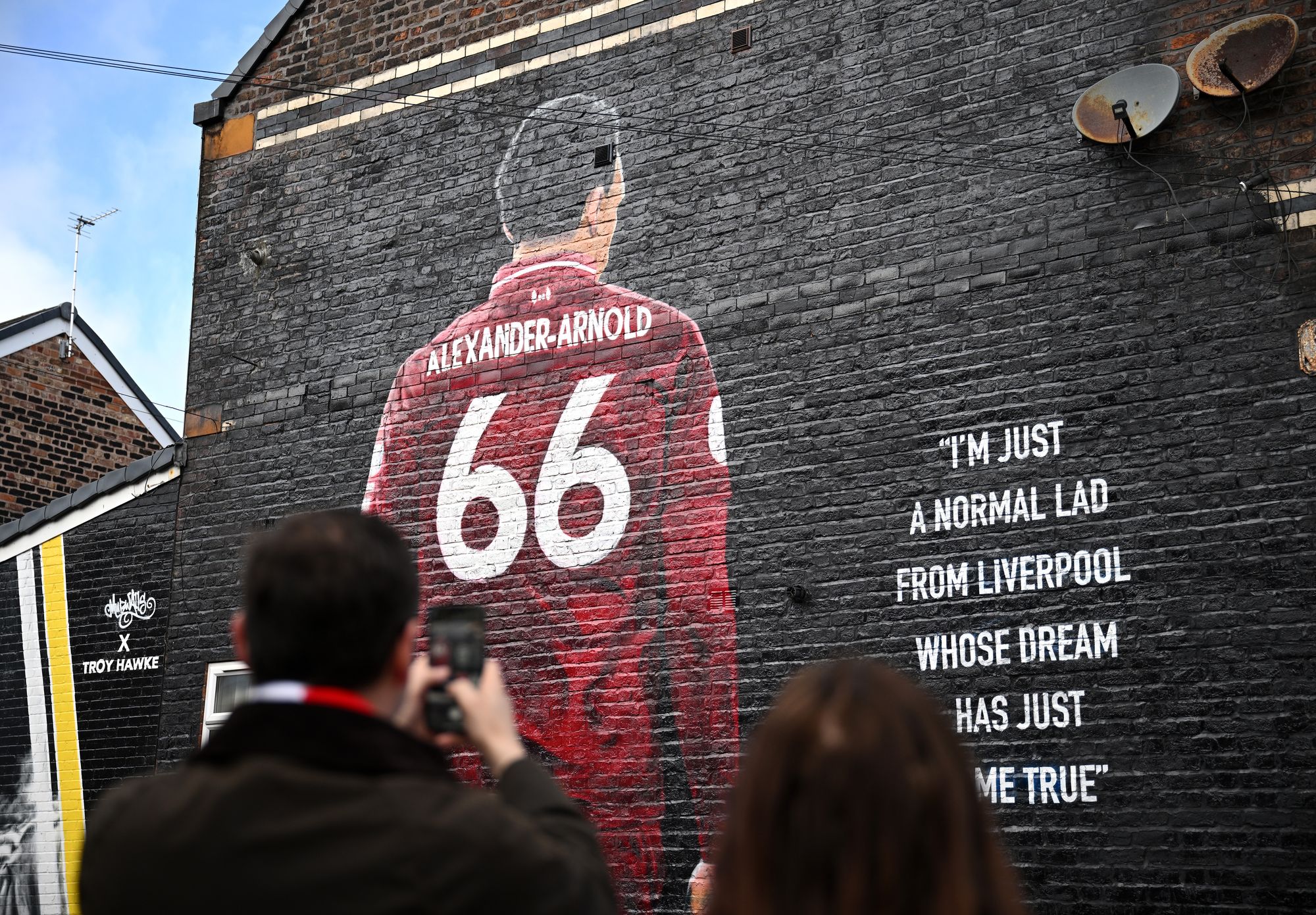 Fans of Liverpool take a picture of a mural which features Trent Alexander-Arnold