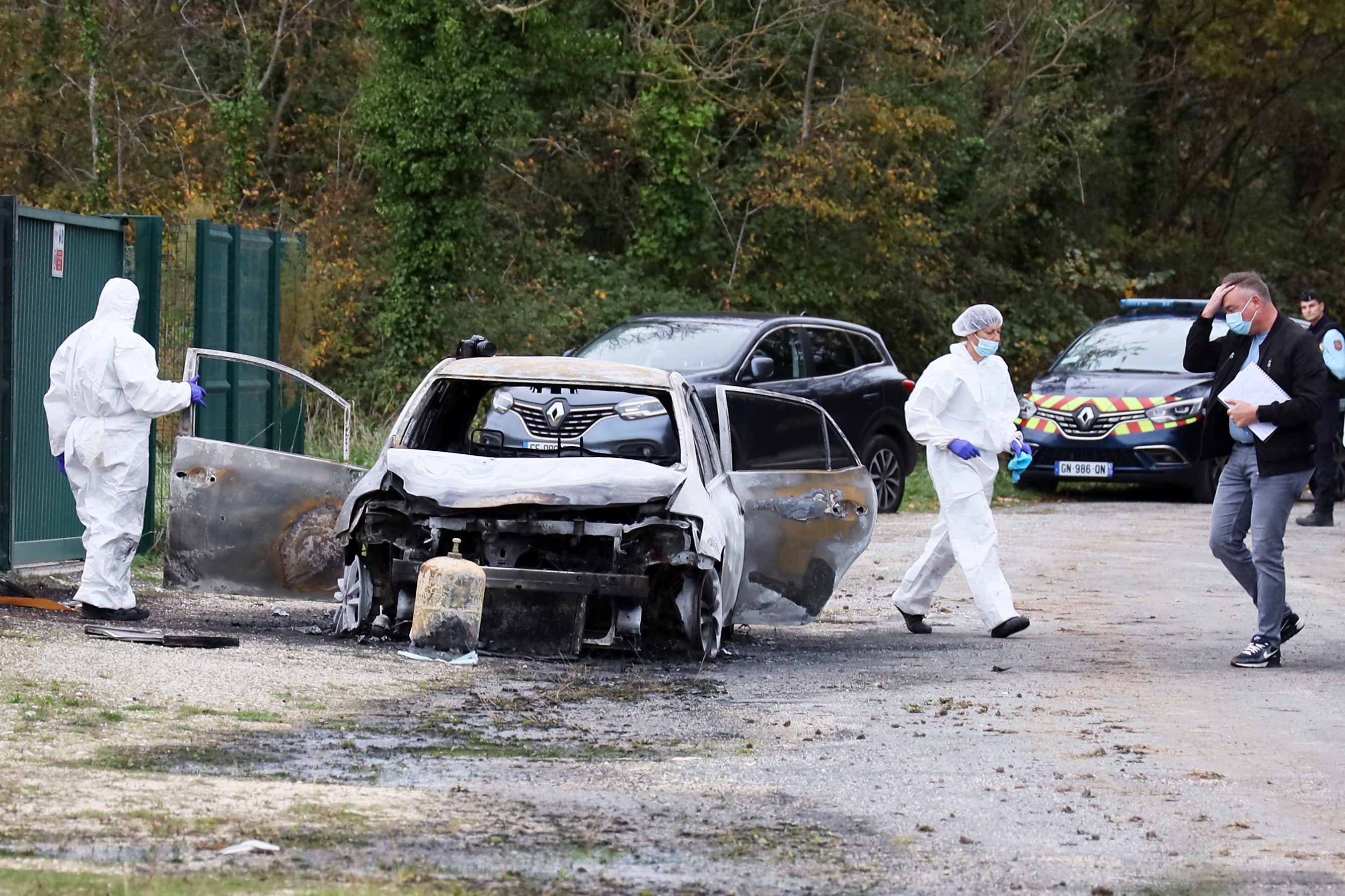 <p>Investigators inspect the burned car after a motorist deliberately rammed pedestrians in France</p>