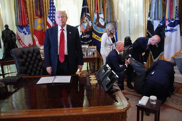 <p>El presidente Donald Trump permanece de pie mientras los asistentes ayudan a un hombre que se desplomó durante un evento sobre la reducción de los precios de los medicamentos en la Oficina Oval el jueves</p>
