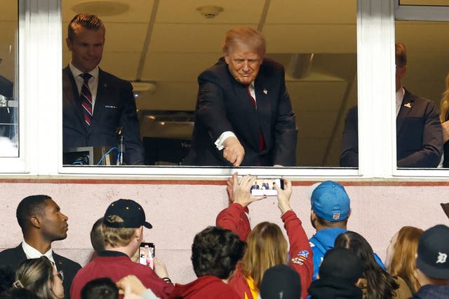 <p>Donald Trump gestures to fans while standing next to U.S. Secretary of War Pete Hegseth (L) after swearing in a new group of U.S. military recruits during halftime of the game between the Detroit Lions and Washington Commanders </p>
