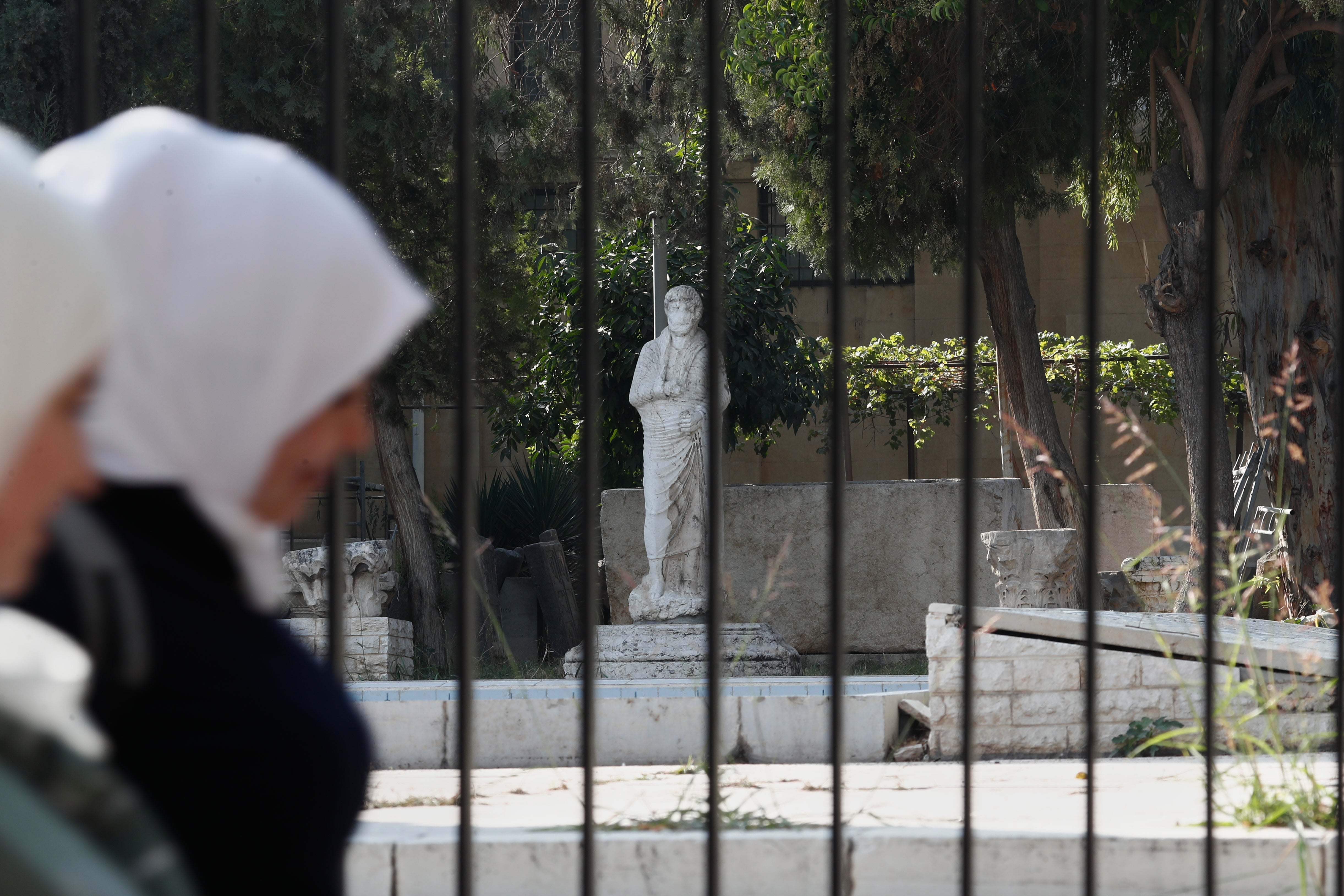 Syrian women walk past a fence of the National Museum of Syria in Damascus, Syria, where the treasures were stolen from