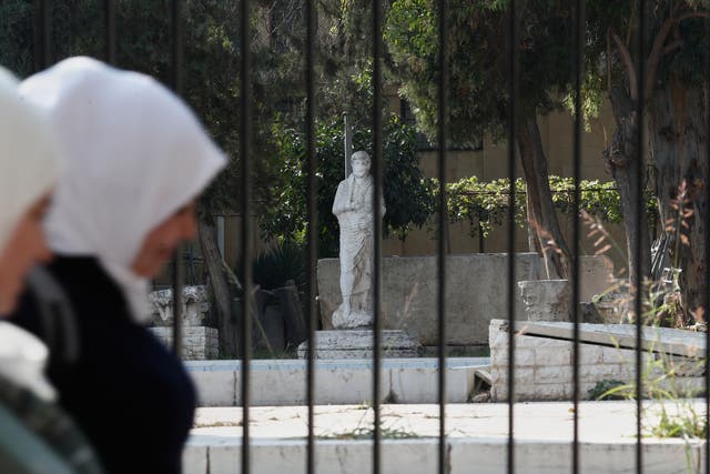 <p>Syrian women walk past a fence of the National Museum of Syria in Damascus, Syria, where the treasures were stolen from</p>