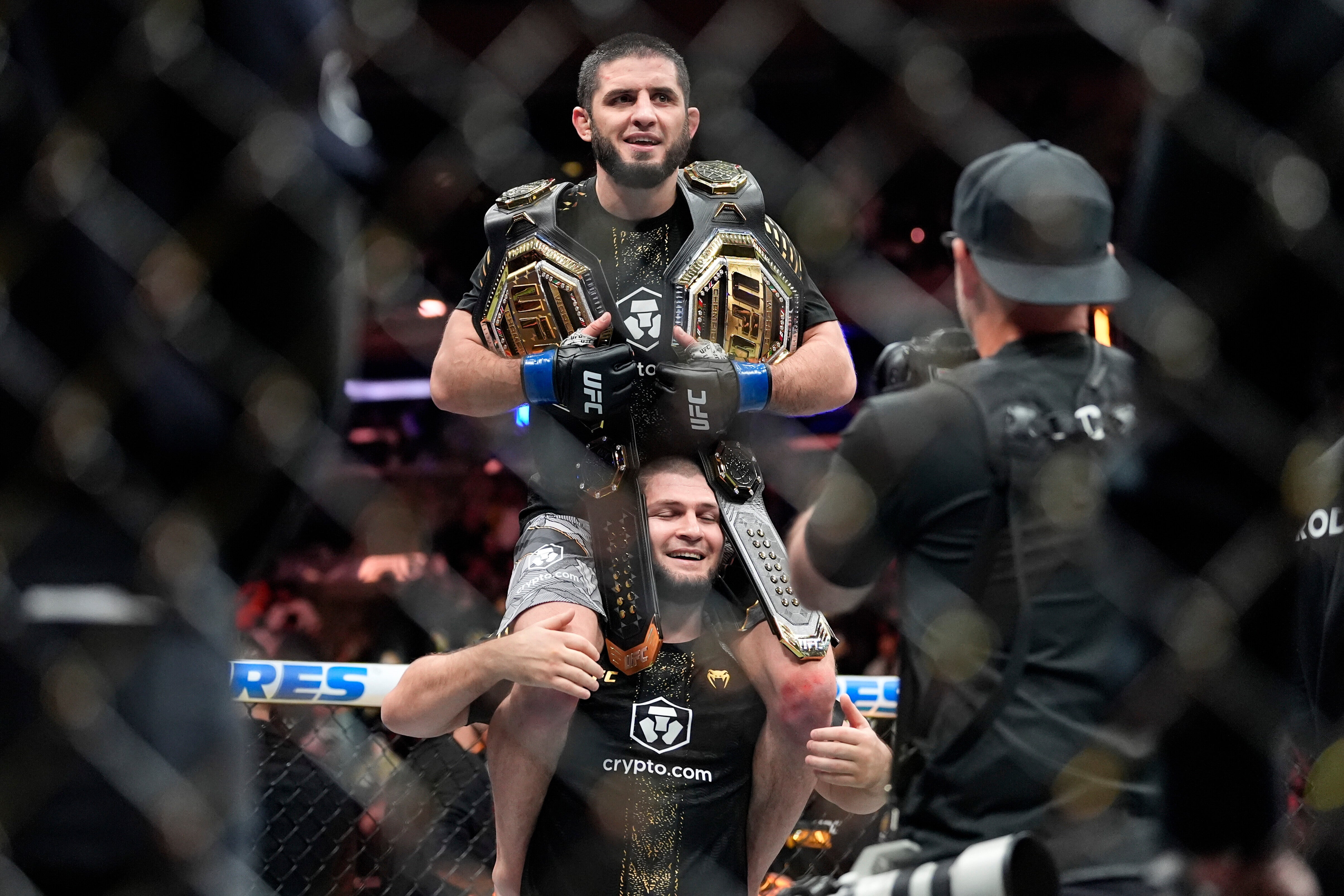 <p>Khabib Nurmagomedov holds Islam Makhachev aloft with his two belts</p>