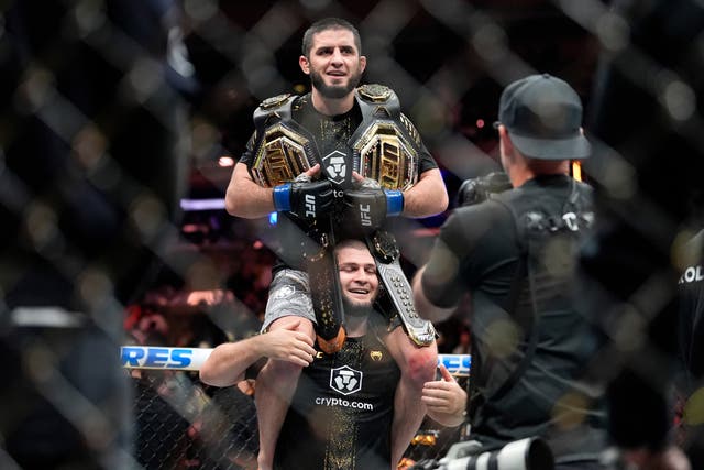 <p>Khabib Nurmagomedov holds Islam Makhachev aloft with his two belts</p>