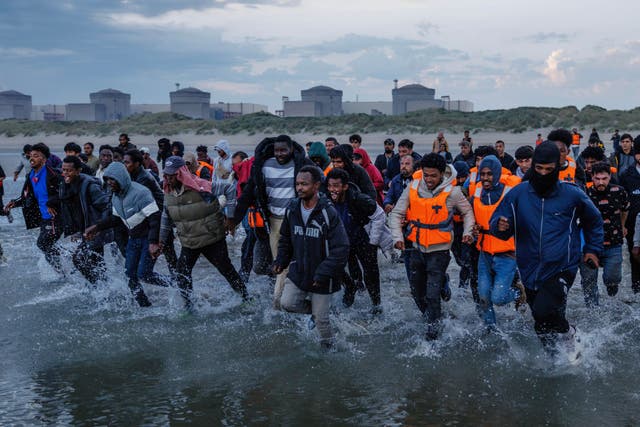 <p>Migrants wade into the water in an attempt to board a small boat on the shoreline in northern France</p>