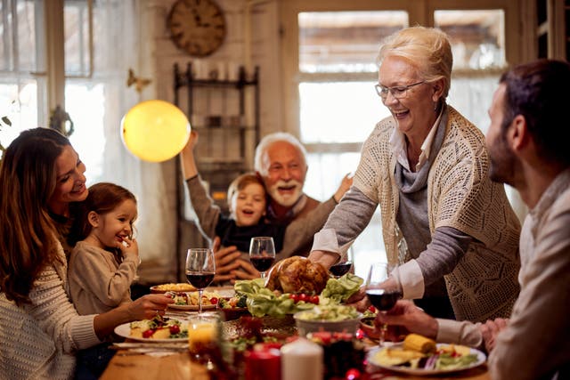 <p>Happy mature woman serving food to her family during Thanksgiving meal at dining table.</p>