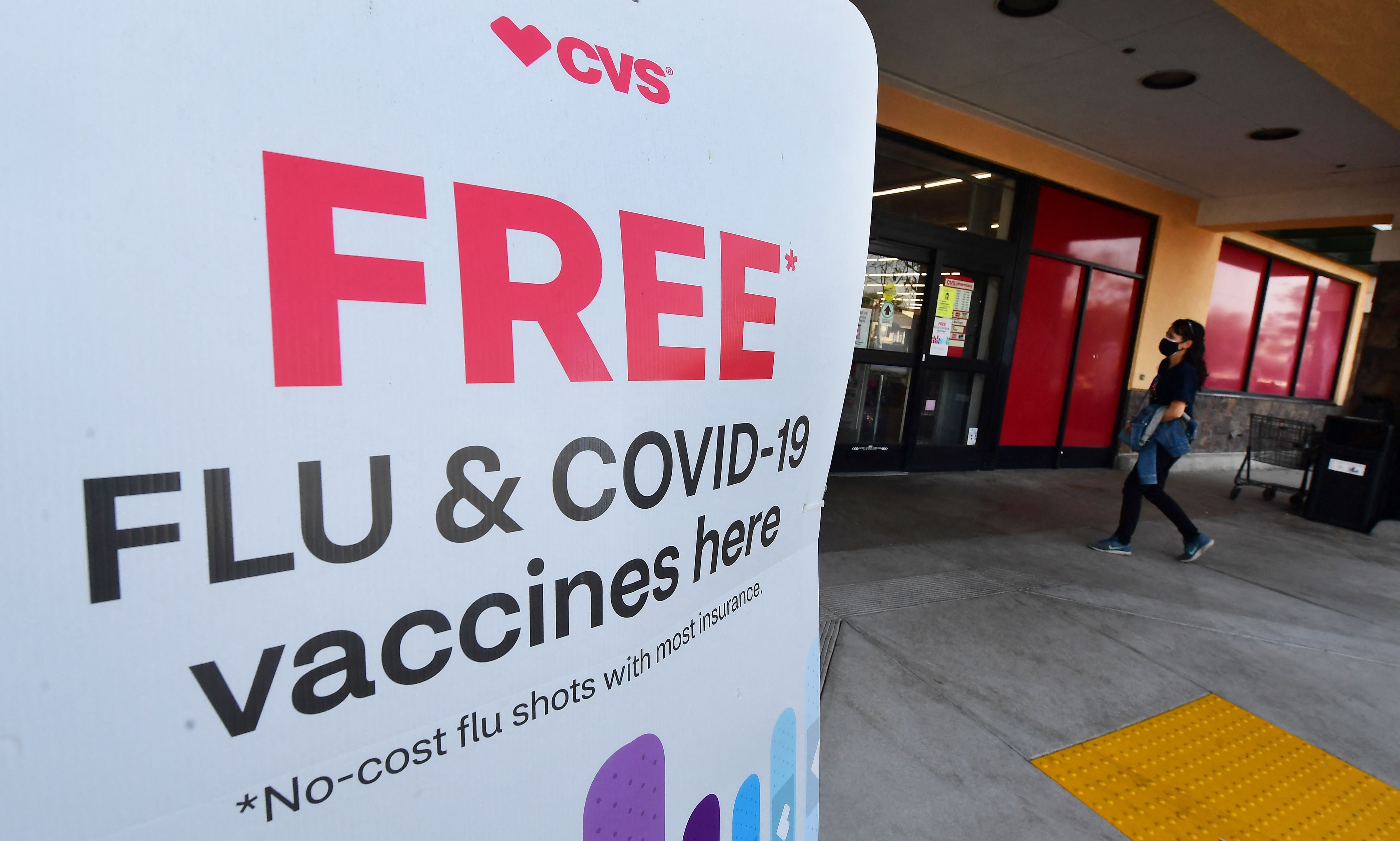 A woman arrives at a CVS pharmacy past a sign about free flu and Covid-19 vaccines on January 14, 2022 in Monterey Park, California.