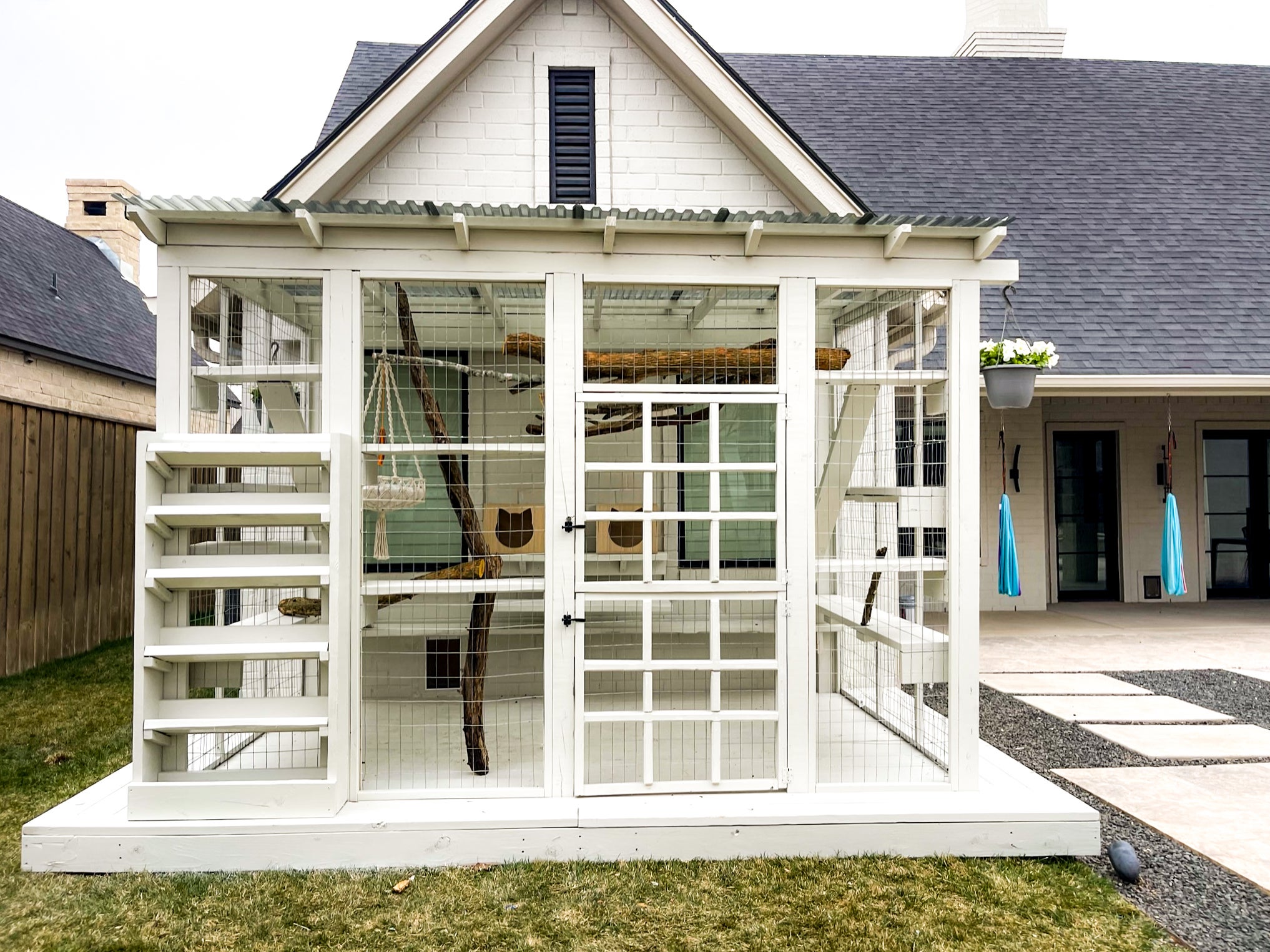 A white, roofed catio with stairs and tree bark inside for the cat to climb on, built outside a home in Texas