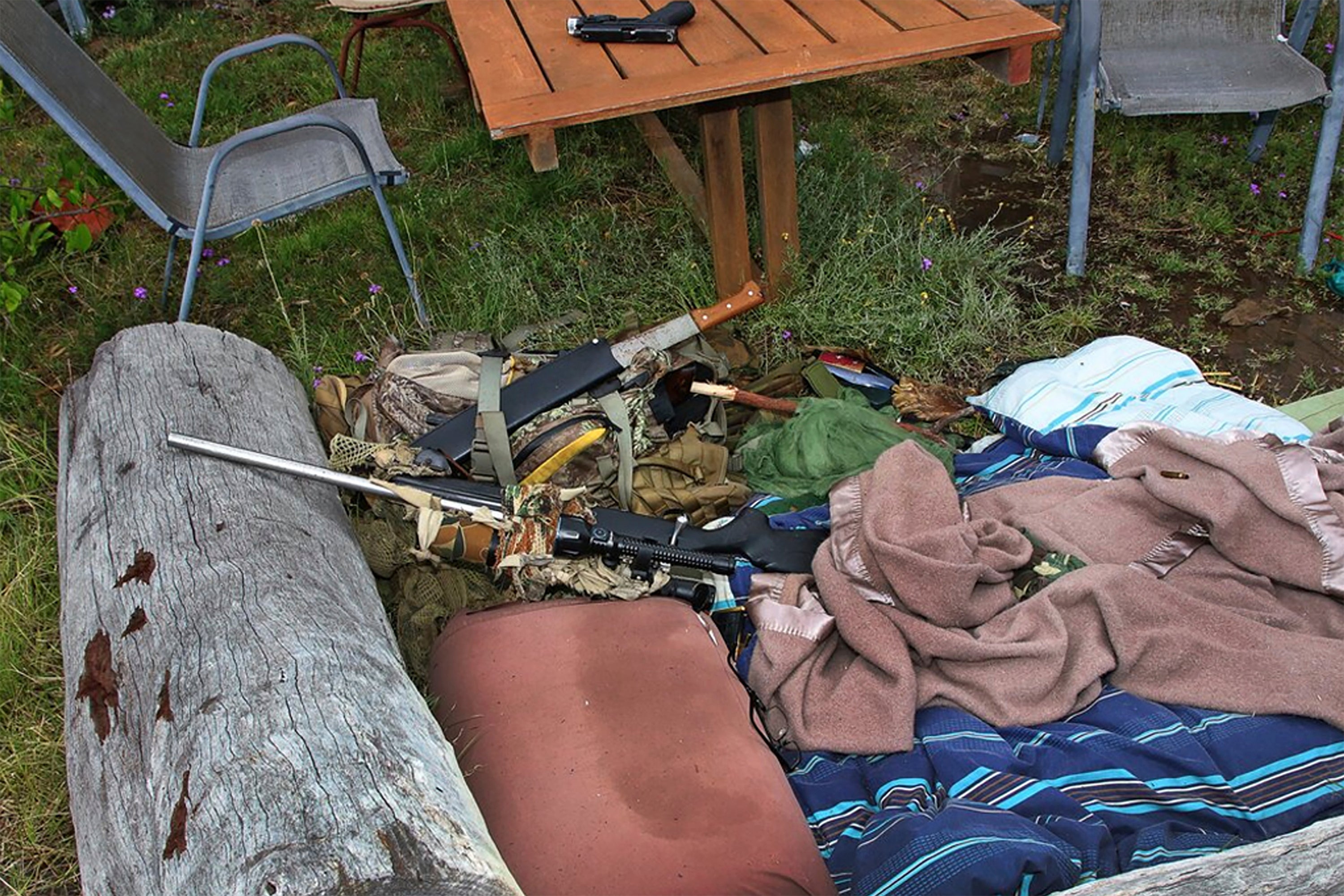 In this undated photo provided by the Queensland Department of Justice and Attorney-General, a rifle lays on a log and a pistol is on a near-by table at a rural property in Wieambilla, Australia