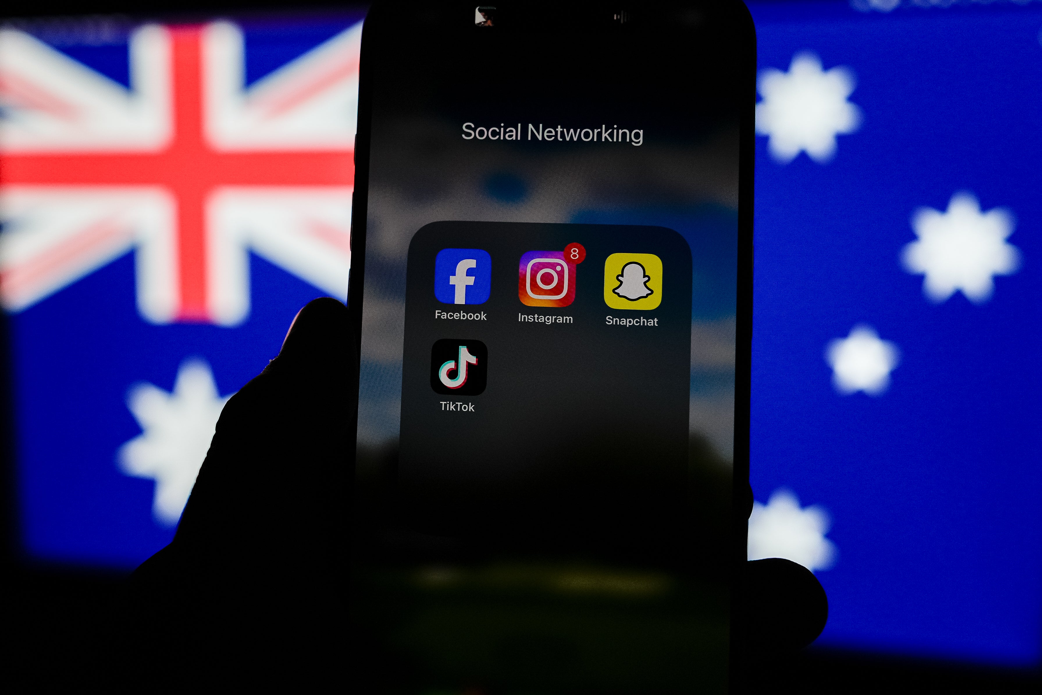 Social media networking apps are displayed on a phone screen with the Australian flag displayed in the background