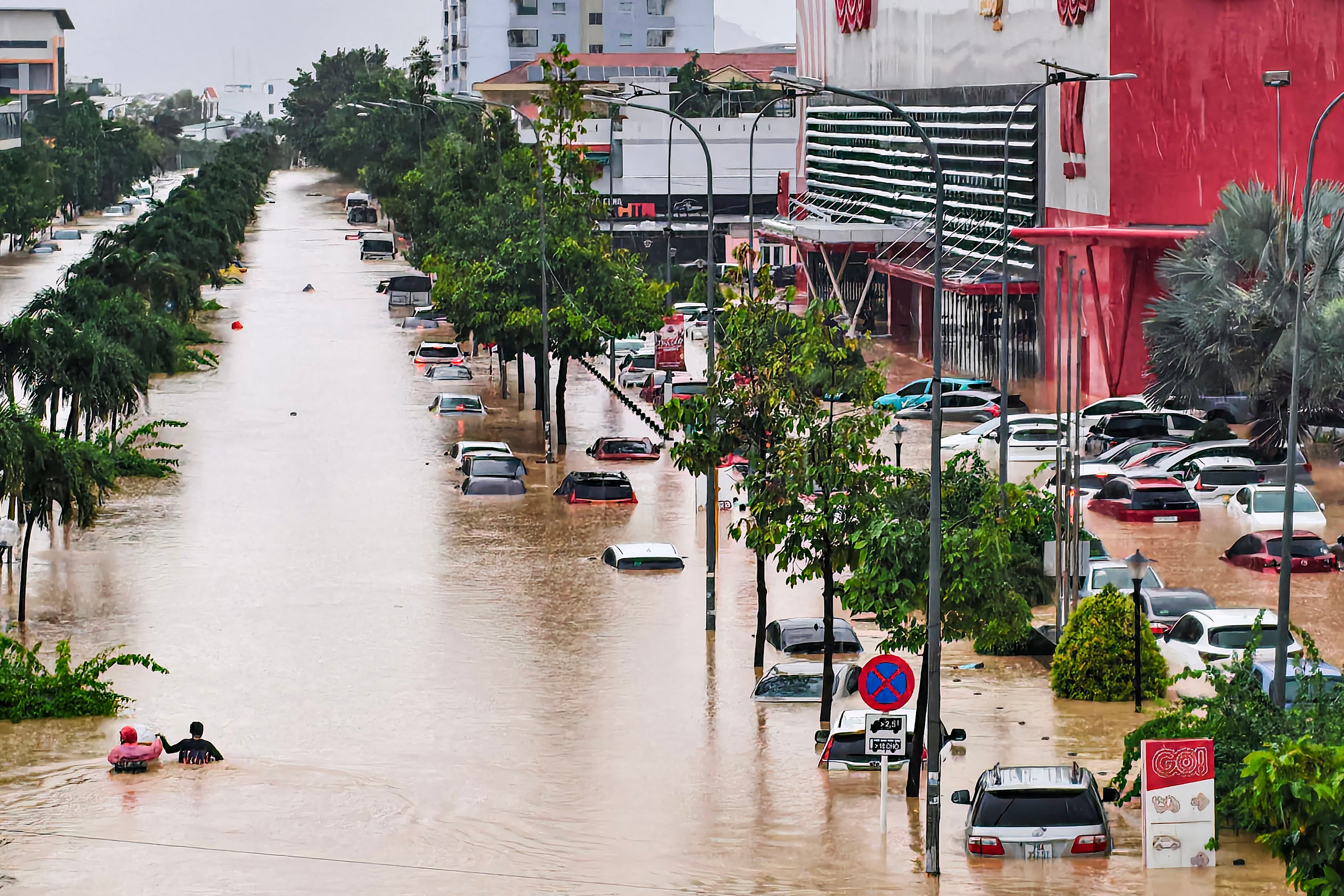 Pessoas (L) caminham pelas enchentes perto de veículos inundados em Nha Trang, província costeira de Khanh Hoa, no Vietnã, em 20 de novembro de 2025. O número de mortos após uma semana de chuvas torrenciais que causaram inundações e deslizamentos de terra no centro do Vietnã aumentou para 16, enquanto milhares de casas foram inundadas em 
