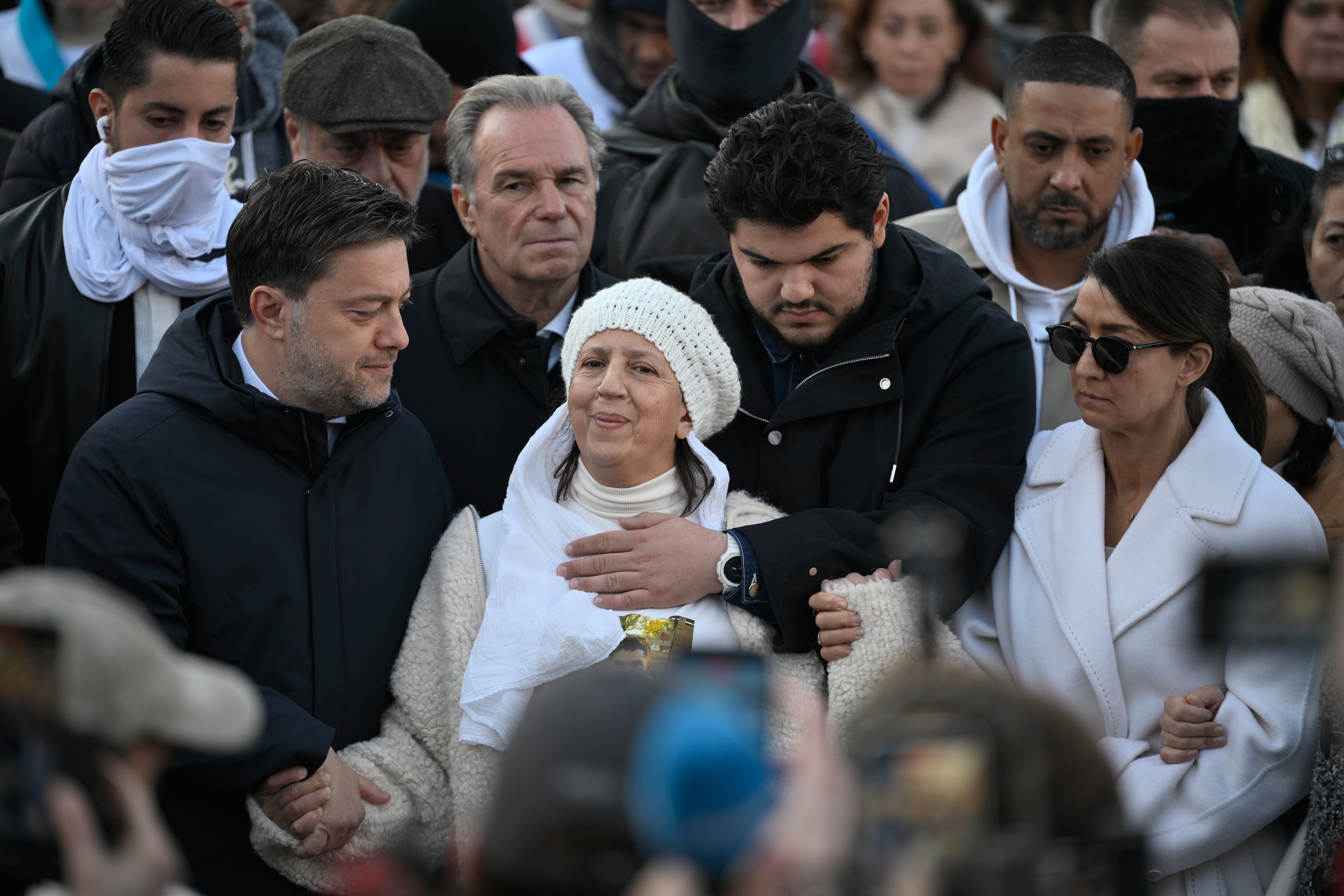 Amine Kessaci, center, and his mother attend a gathering in homage to his brother Mehdi Kessaci at the roundabout where he was murdered, and to protest against drug trafficking, in Marseille, southern France, Saturday, Nov. 22, 2025. (AP Photo/Philippe Magoni)
