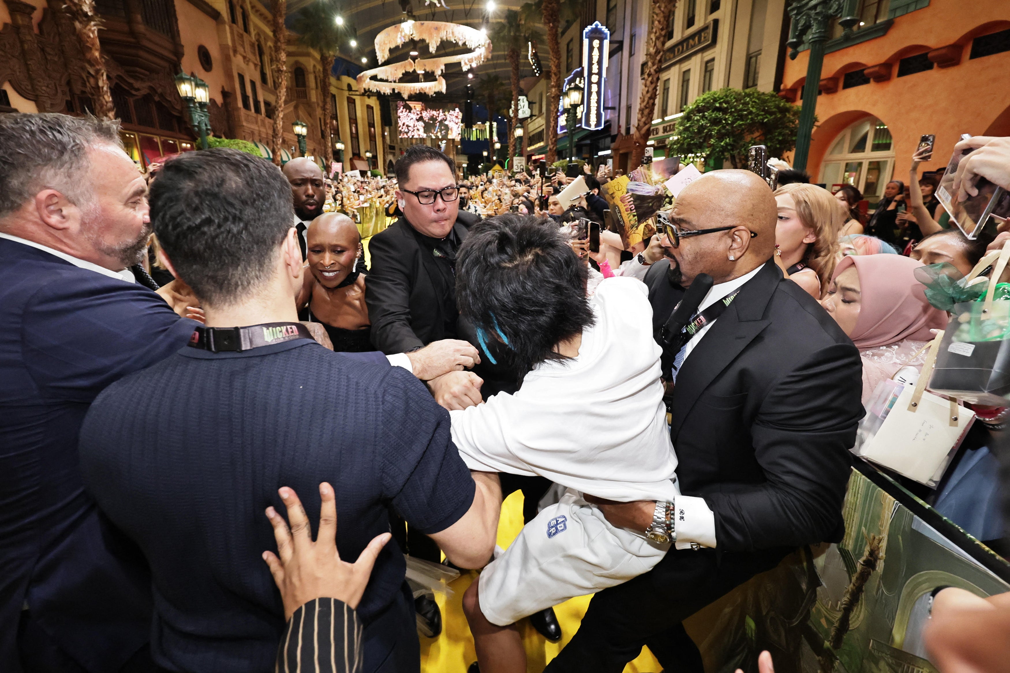 <p>This picture by The Straits Times taken November 13, 2025 and provided on November 14 shows a man (C) accused of attacking pop star Ariana Grande being grabbed by security guards as co-star Cynthia Erivo (3rd L) reacts at the premiere of their film "Wicked: For Good" in Singapore</p>
