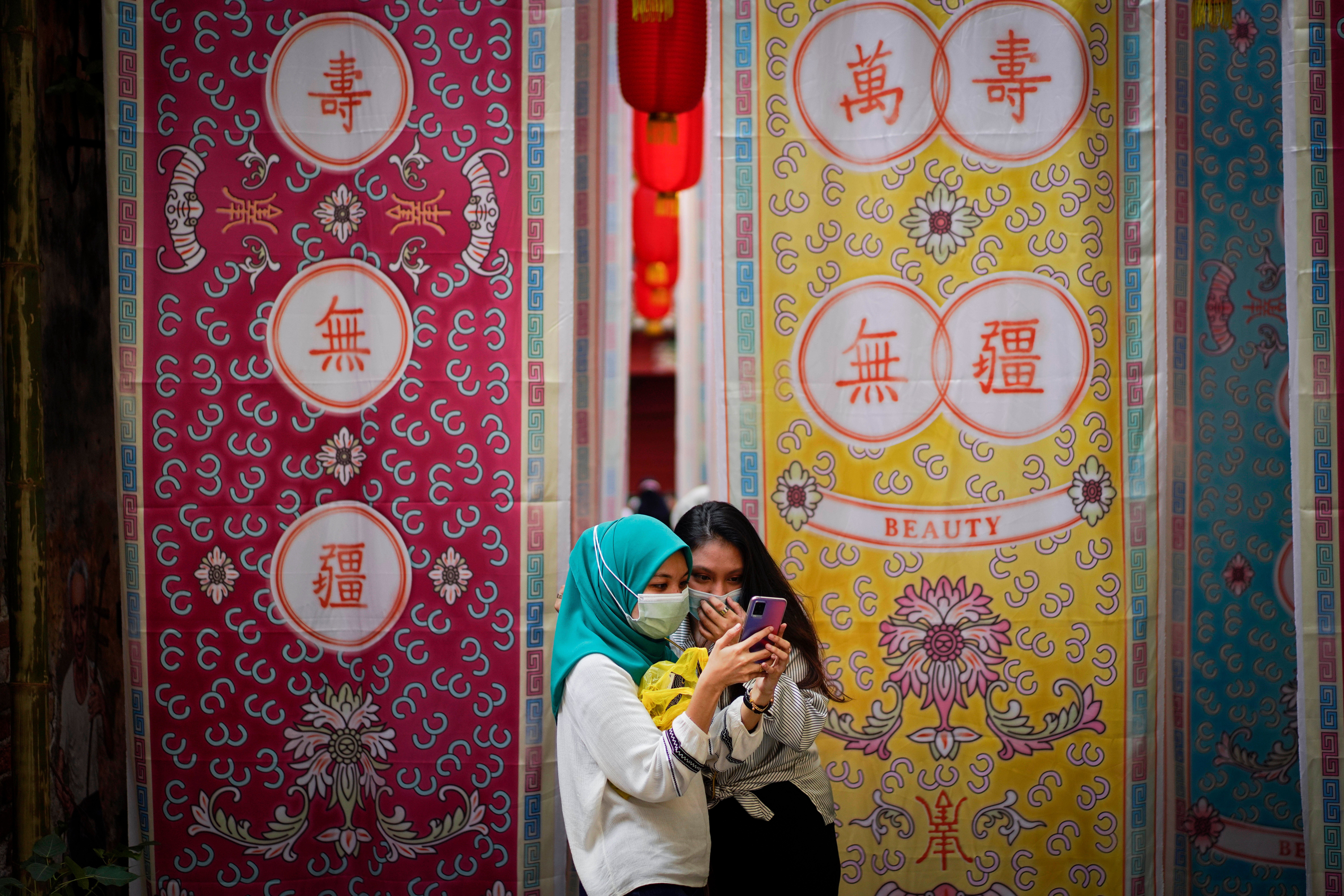 Two Malay girls check a mobile phone at a fabric installation decoration at Kwai Chai Hong, the Chinatown area in downtown Kuala Lumpur, Malaysia, Tuesday, March 30, 2021. (AP Photo/Vincent Thian, File)