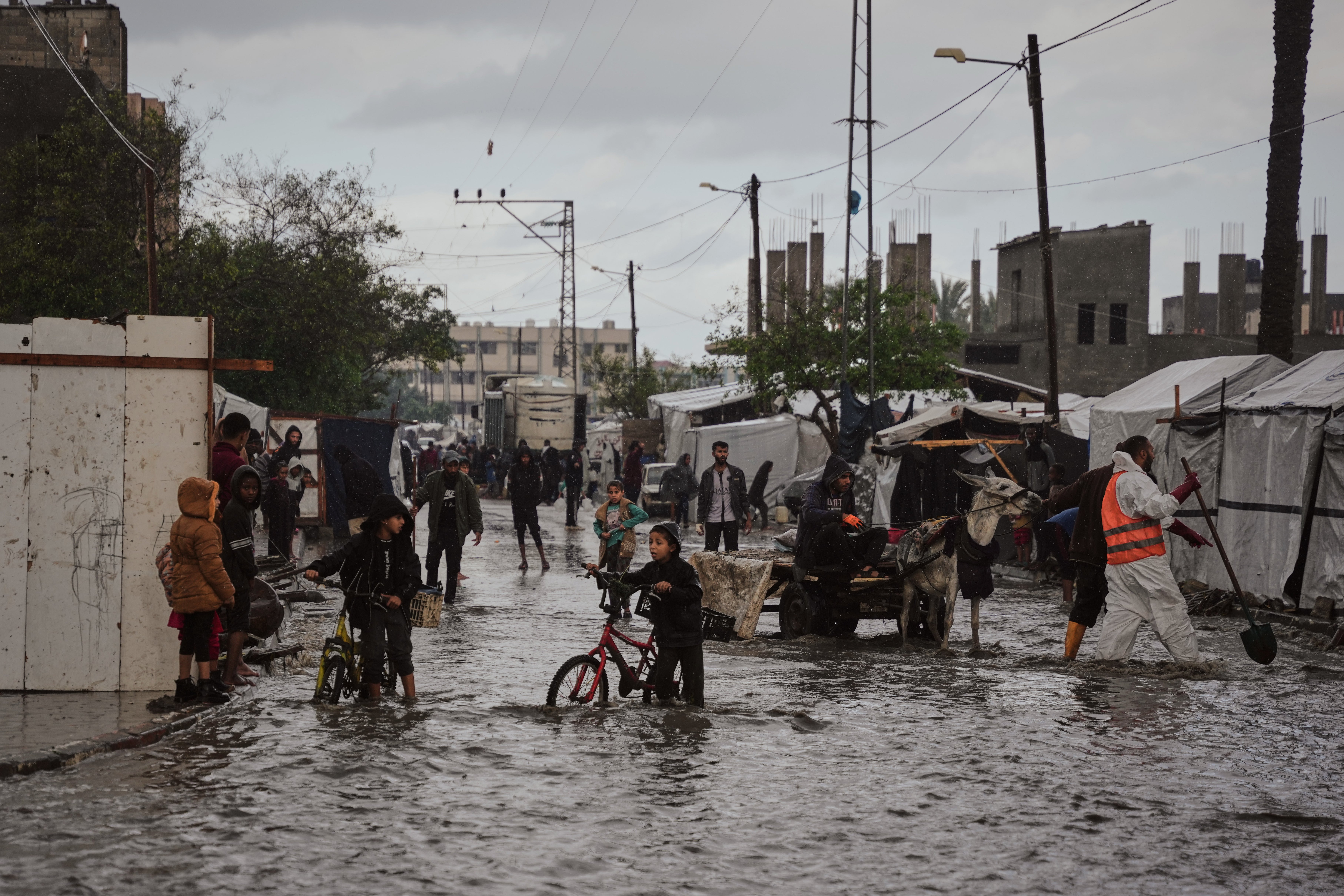 Palestinians walk through a flooded street next to a temporary tent camp after heavy rainfall in Deir al-Balah, central Gaza Strip
