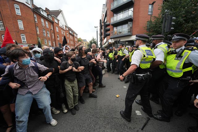 <p>Police form a barrier in front of masked protesters outside the Thistle City Barbican Hotel in central London, which houses asylum seekers in August 2025</p>