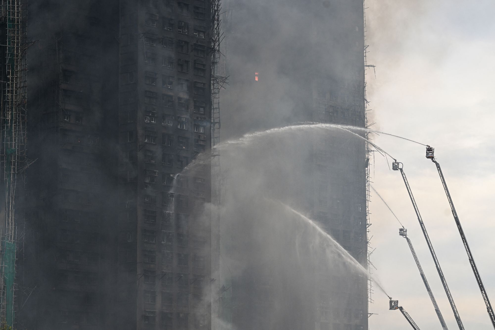 Firefighters spray water on flames as a major fire burns through several apartment blocks at the Wang Fuk Court residential estate